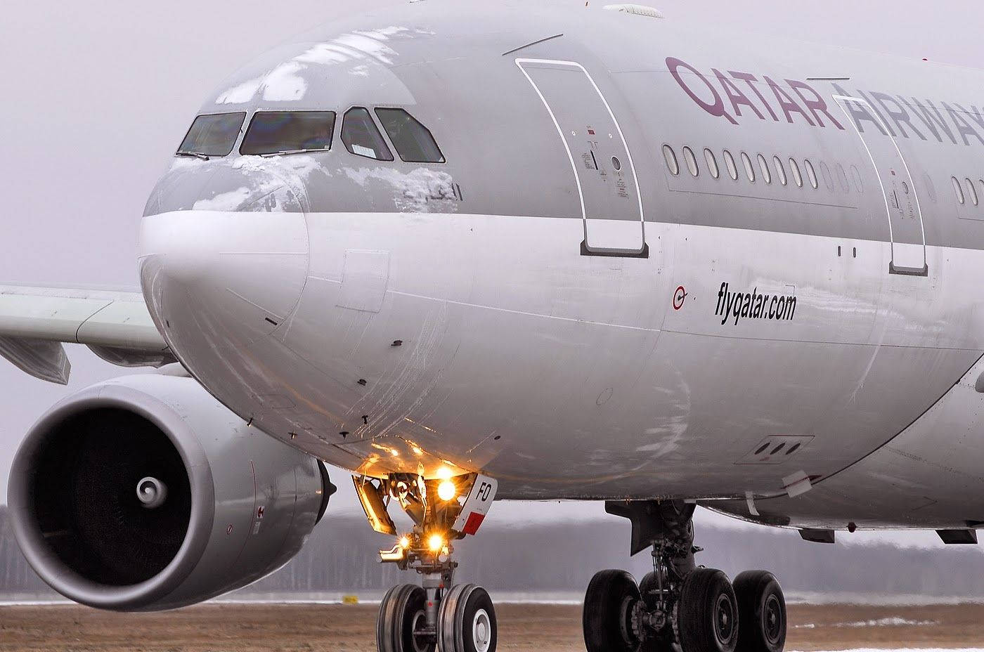 Qatar 桌布 壁紙 — 卡達航空飛機在積雪跑道上的特寫，起落架燈溫暖地亮著。