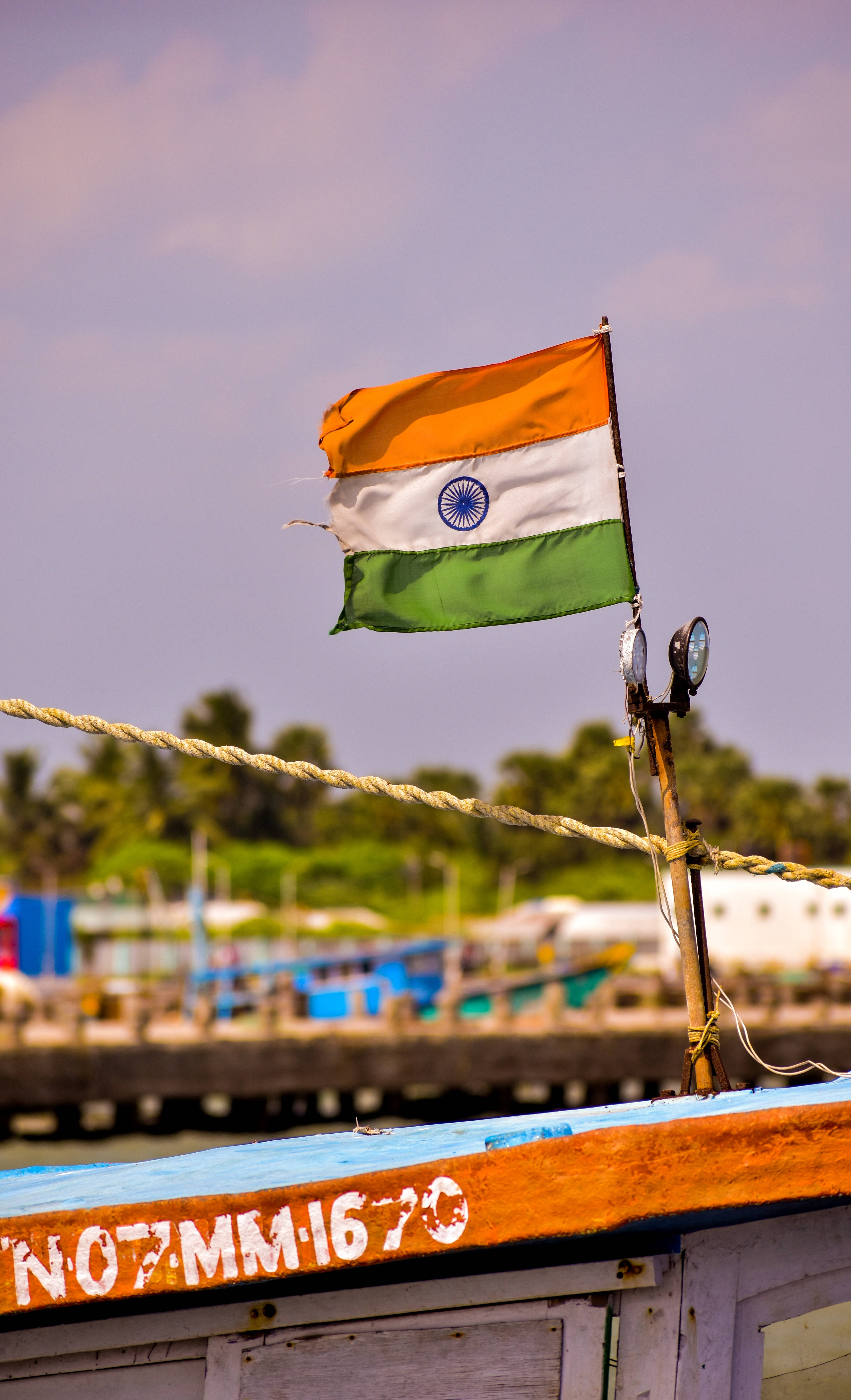 Tiranga 桌布 壁紙 — 印度國旗在一艘停泊在熱帶港口、飽經風霜的木船上自豪地飄揚，背景是茂密的綠色植物。