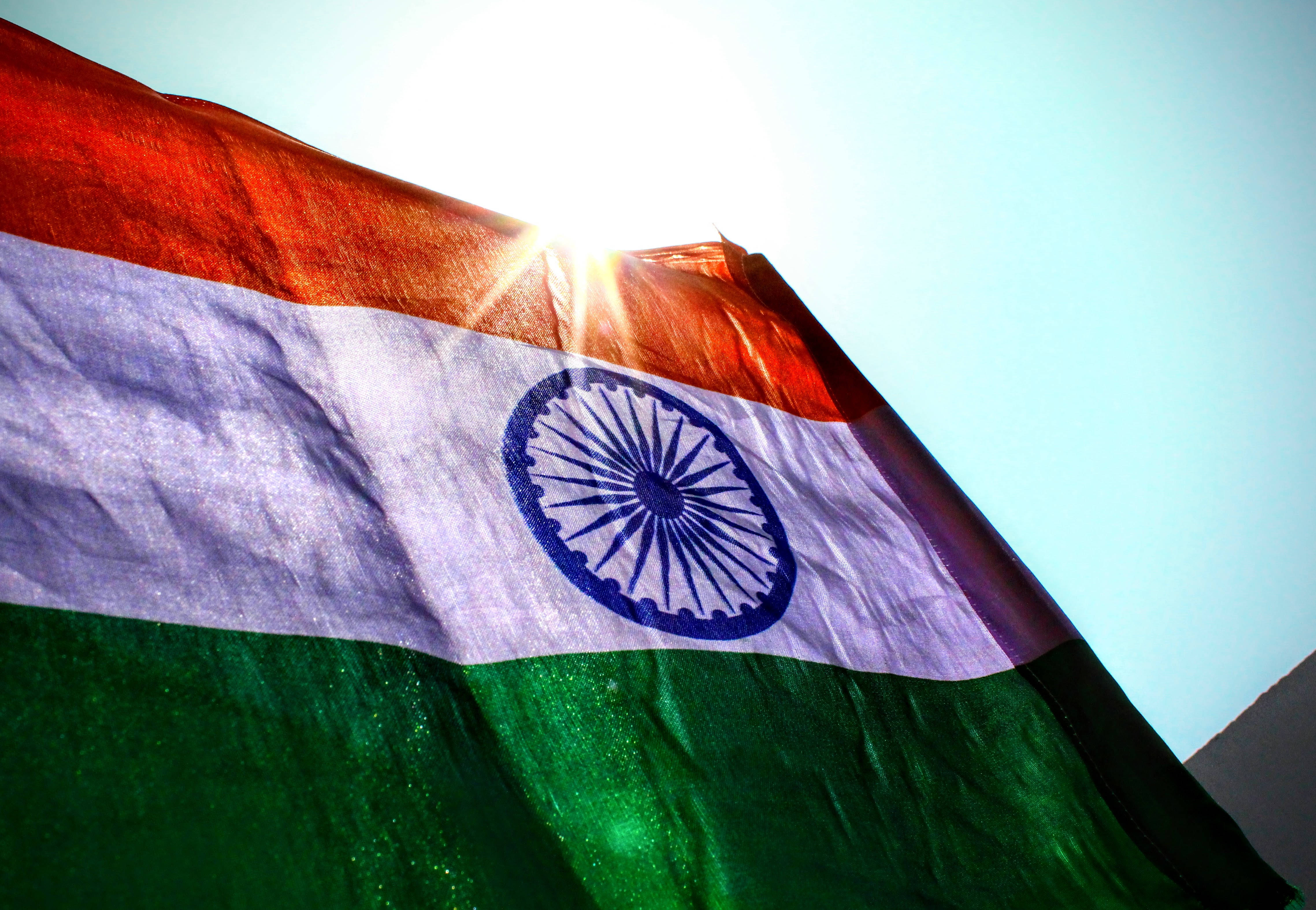 Indian 桌布 壁紙 — 印度國旗在明亮的天空下動態飄揚，陽光透過布料褶皺形成光芒四射的效果。