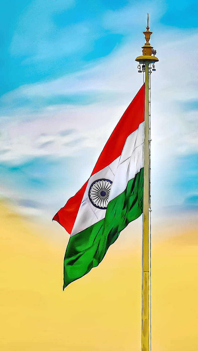 Indian 桌布 壁紙 — 印度國旗在金色旗桿上自豪地飄揚，背景是充滿活力的藍色和黃色天空，伴有柔軟的雲朵。