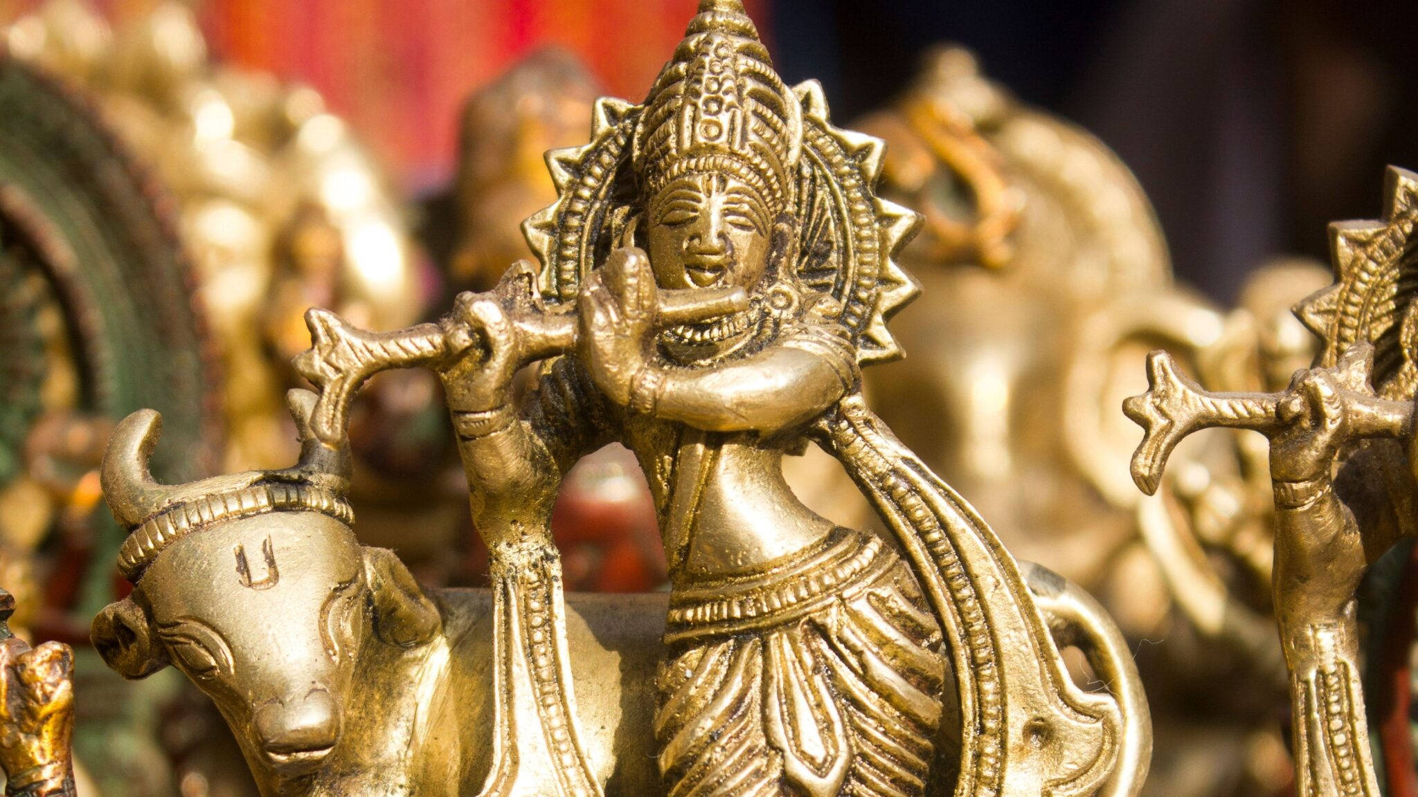 Krishna Desktop 桌布 壁紙 — 印度教神祇克里希納的金色雕像，吹奏長笛騎在牛上，細節精緻，光線溫暖。