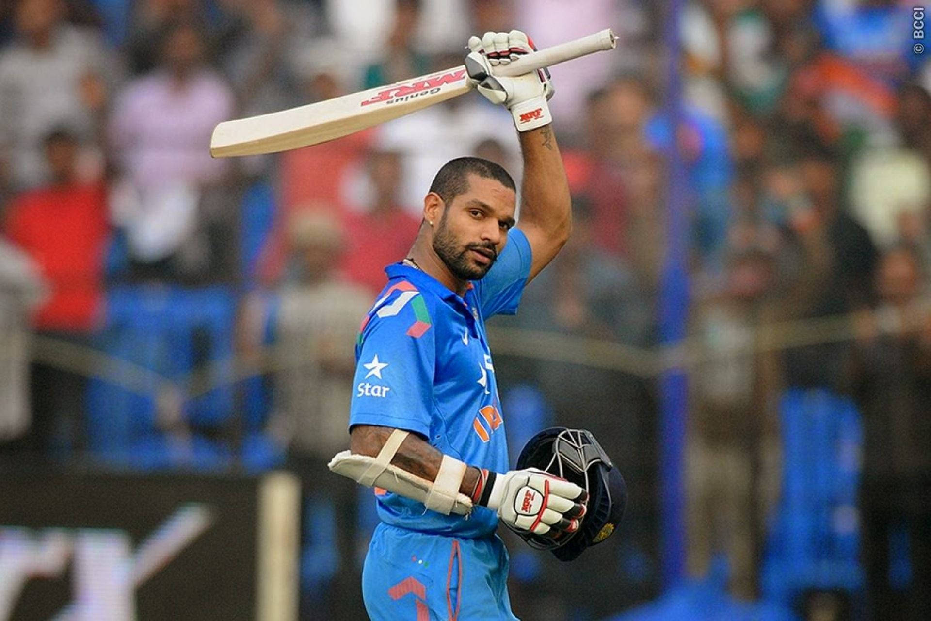 shikhar dhawan 桌布 壁紙 — 印度板球運動員在明亮燈光下的體育場高舉球棒慶祝。
