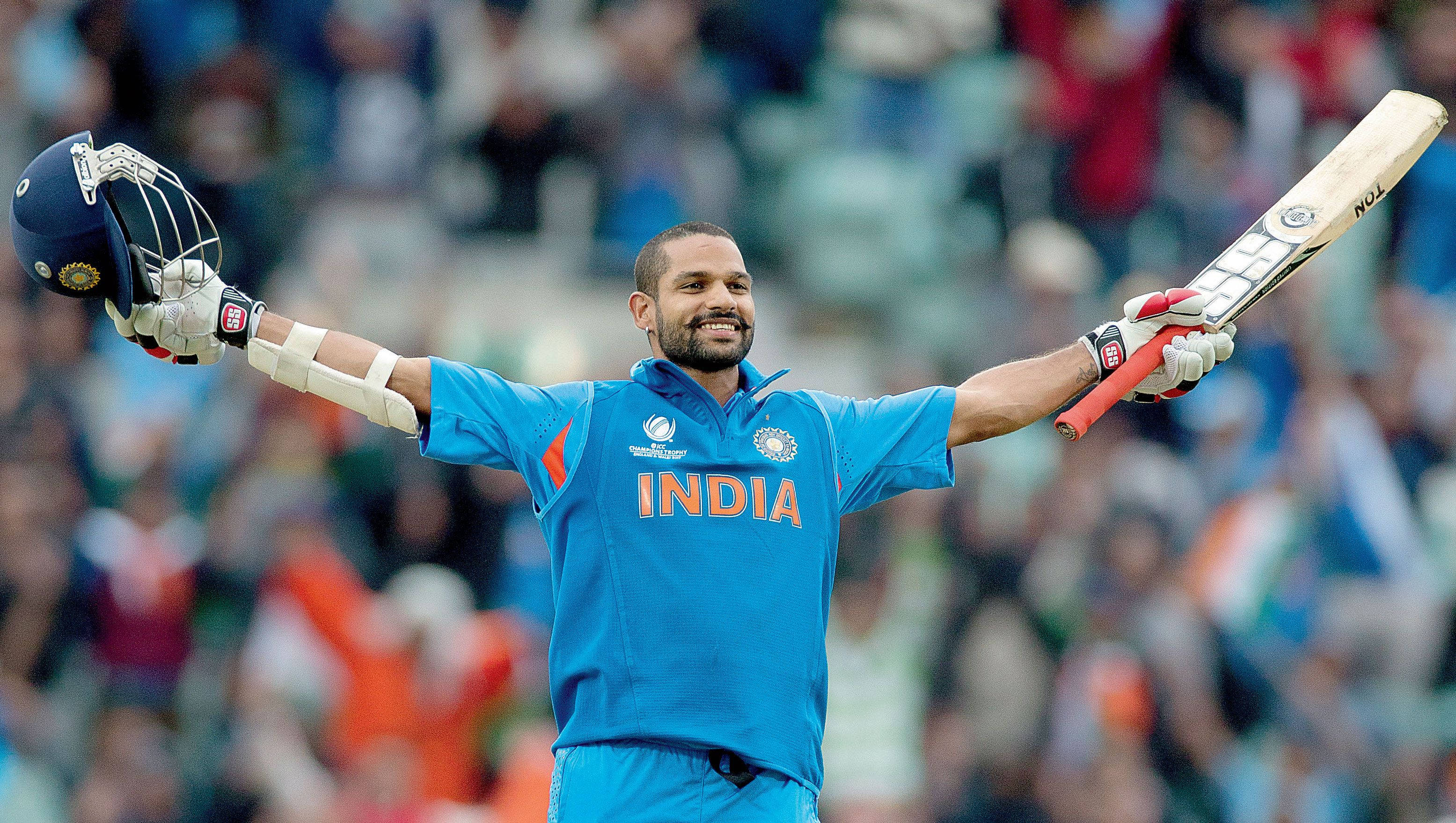 shikhar dhawan 桌布 壁紙 — 印度板球運動員在體育場張開雙臂，高舉球棒和頭盔慶祝勝利。