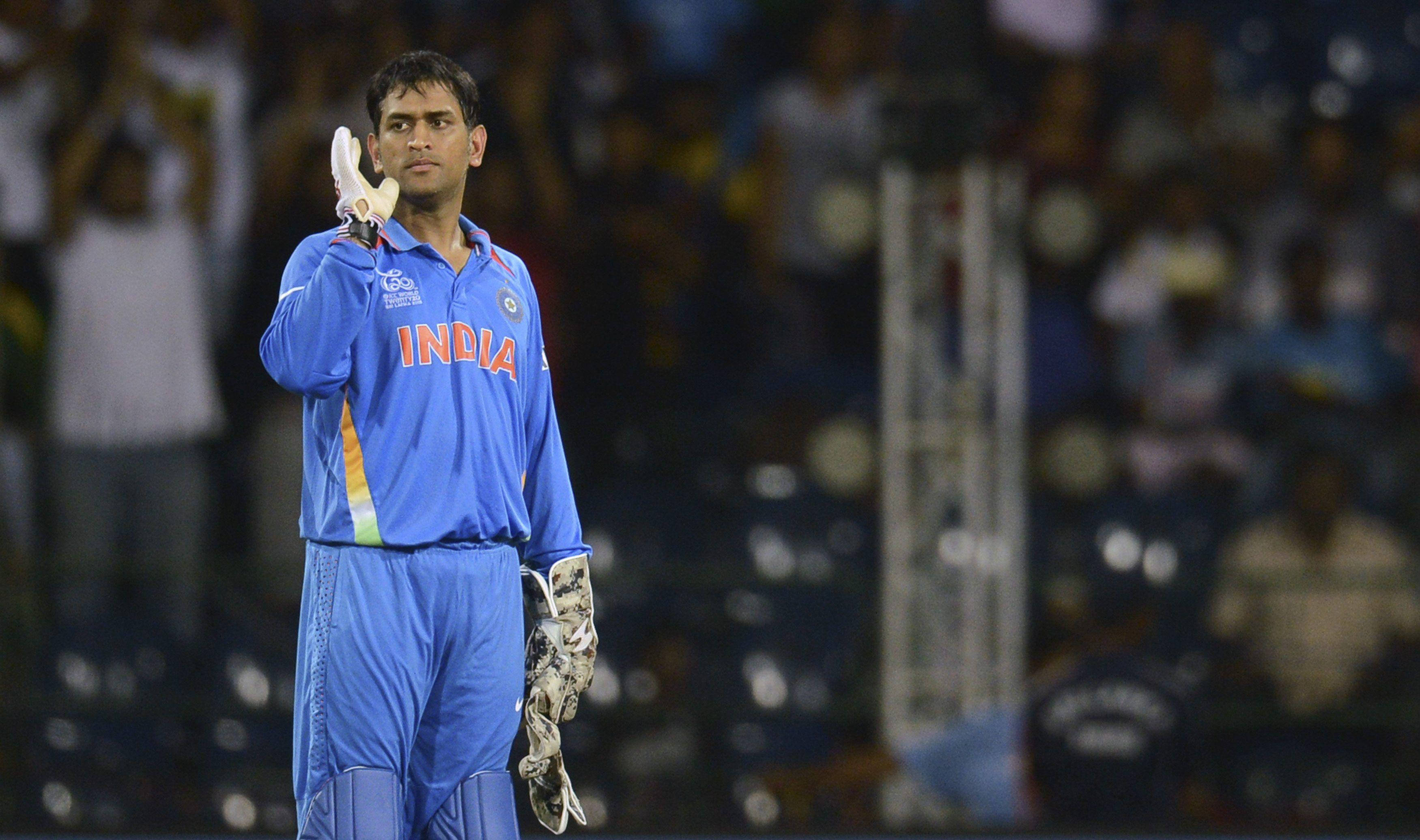 Ms Dhoni 桌布 壁紙 — 印度板球運動員身穿藍色制服在體育場燈光下向人群敬禮，背景有模糊的觀眾。