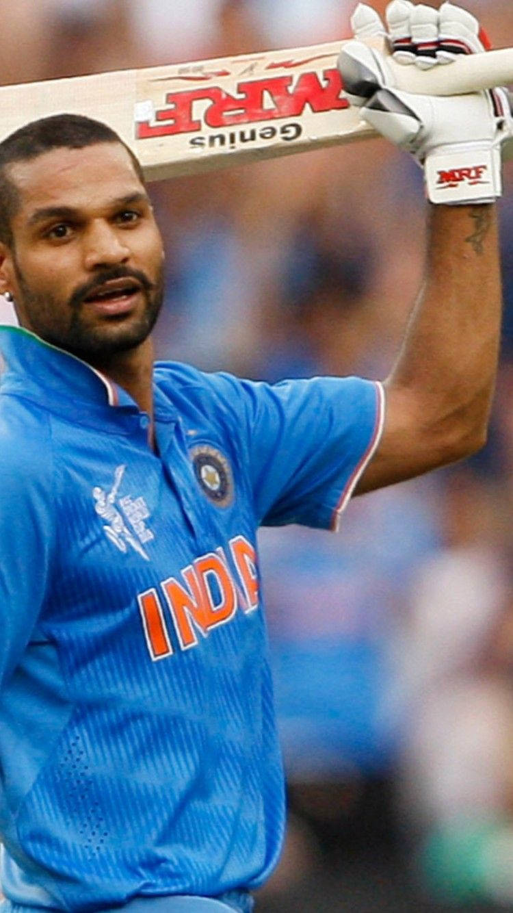 shikhar dhawan 桌布 壁紙 — 印度板球運動員身穿鮮藍色球衣，高舉球棒慶祝勝利。
