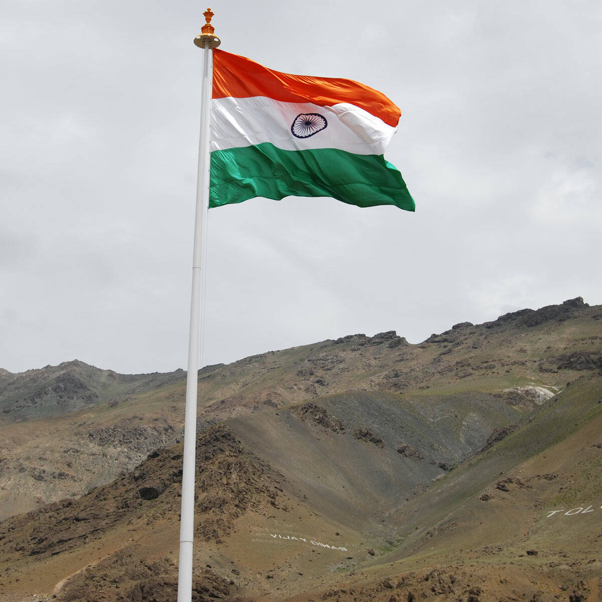 Indian 桌布 壁紙 — 印度的三色旗在陰天背景下，於旗桿上自豪地飄揚，背景是崎嶇貧瘠的山脈。