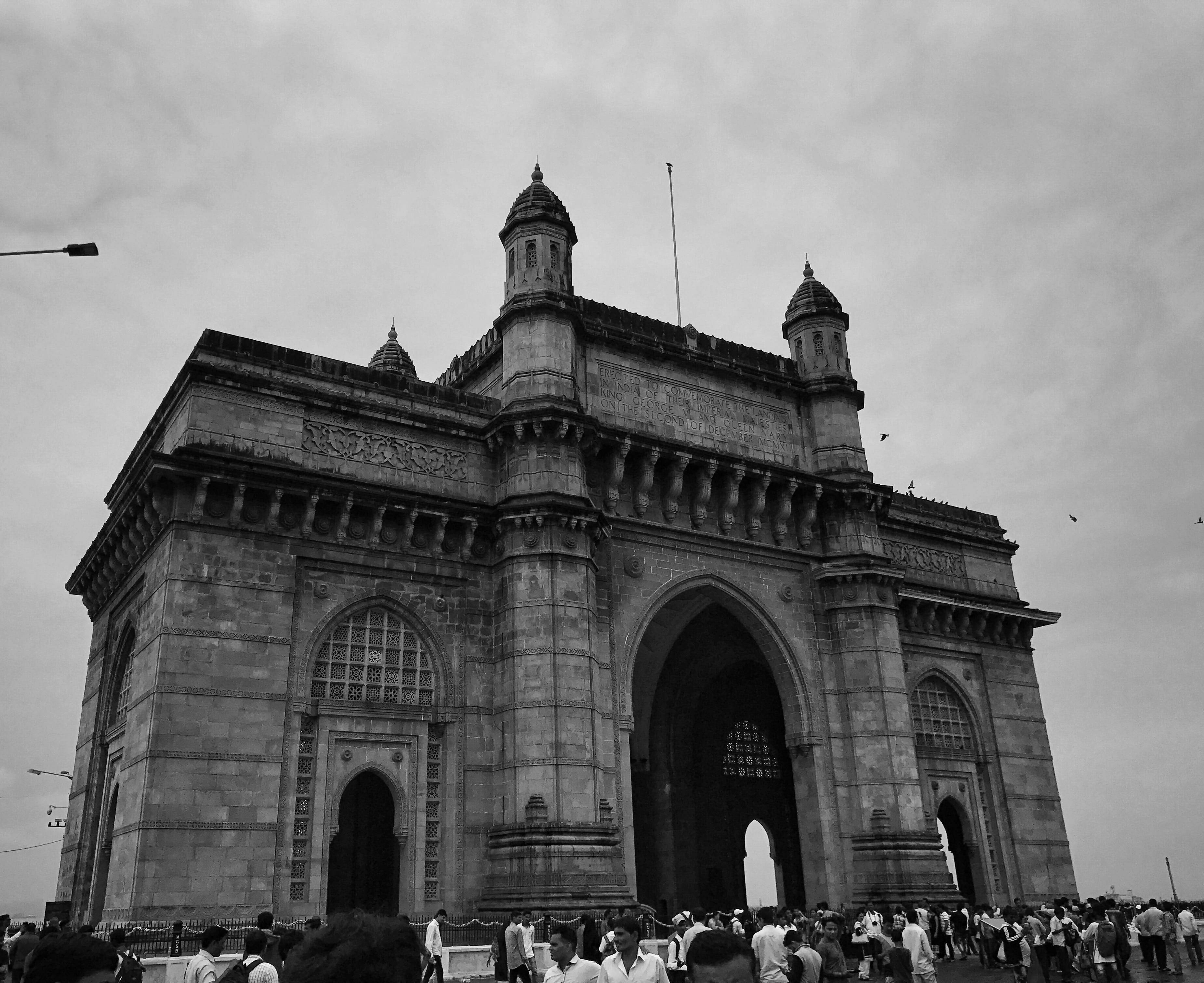 Mumbai 桌布 壁紙 — 印度門紀念碑的單色景觀，人群聚集在其底座下，天空陰沉。