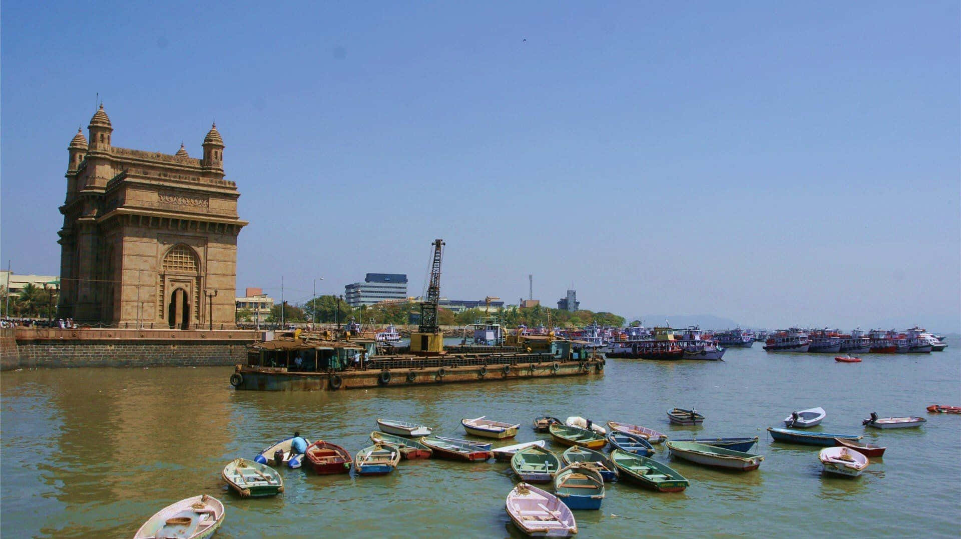 Mumbai 桌布 壁紙 — 印度門雄偉地矗立在海濱，色彩繽紛的船隻在晴朗的藍天下漂浮在港灣中。