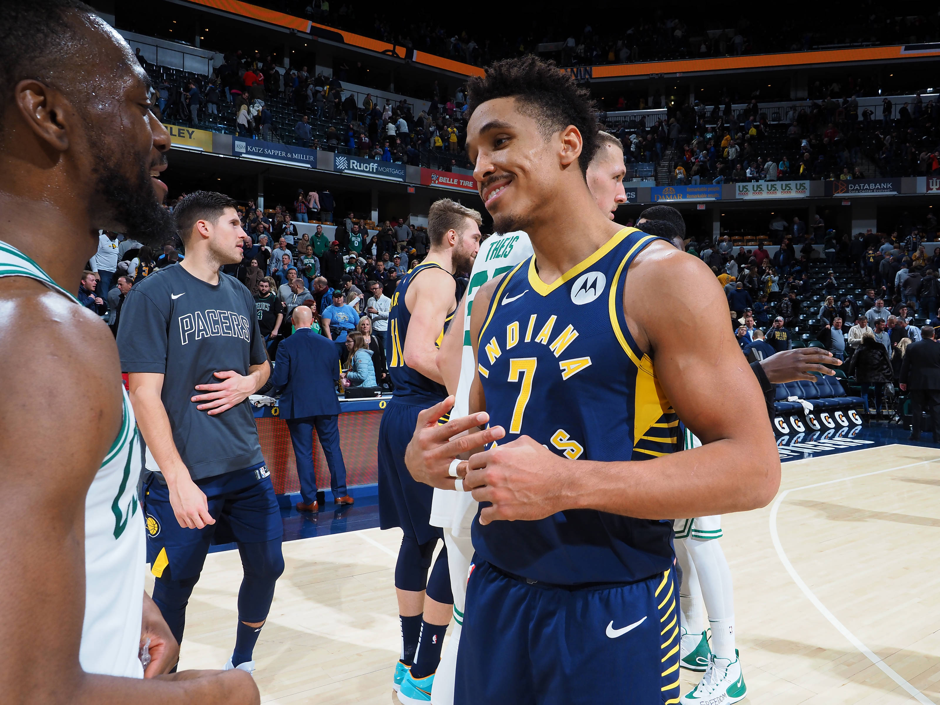 malcolm brogdon 桌布 壁紙 — 印第安納溜馬隊7號球員在比賽期間於燈光明亮的籃球場上與隊友互動，露出溫暖的笑容。