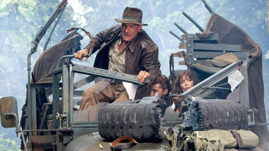 Indiana Jones 桌布 壁紙 — 印第安納瓊斯緊握受損軍用吉普車的方向盤，兩位同伴透過碎裂的擋風玻璃向內觀望。