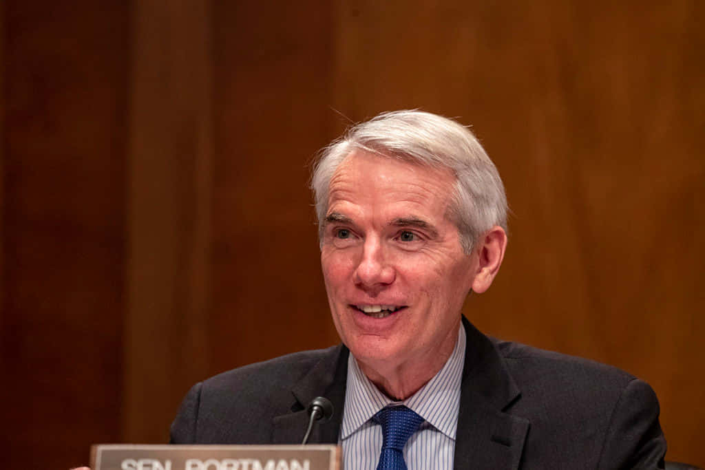 政治 桌布 壁紙 — 參議員 Rob Portman 在正式聽證會上微笑發言，背景為木質牆面。