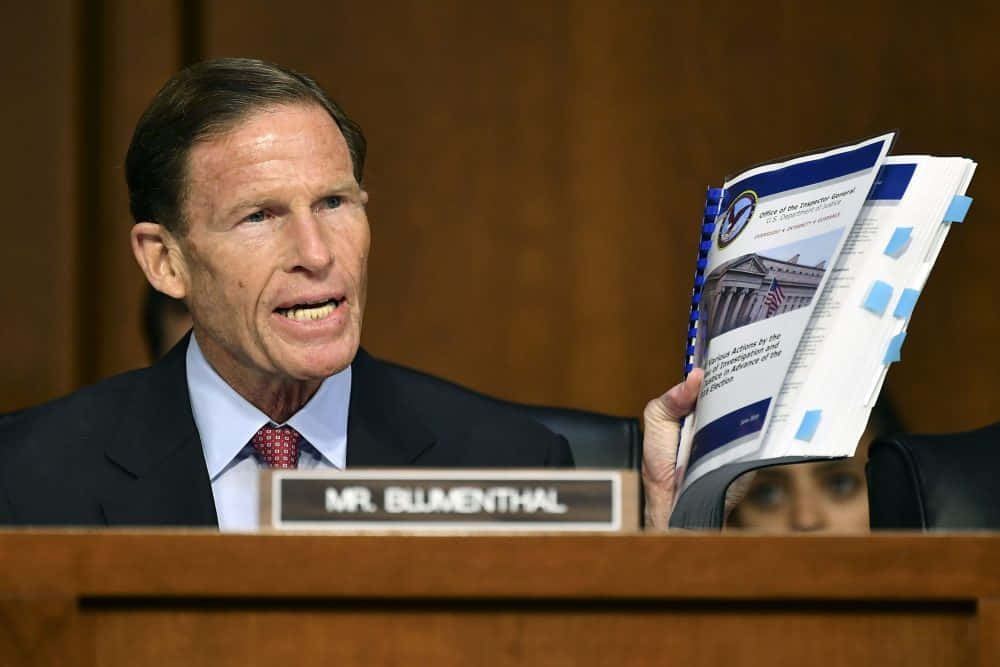 American 桌布 壁紙 — 參議員Richard Blumenthal在正式聽證會上發言，手持一份貼有藍色便利貼的文件。