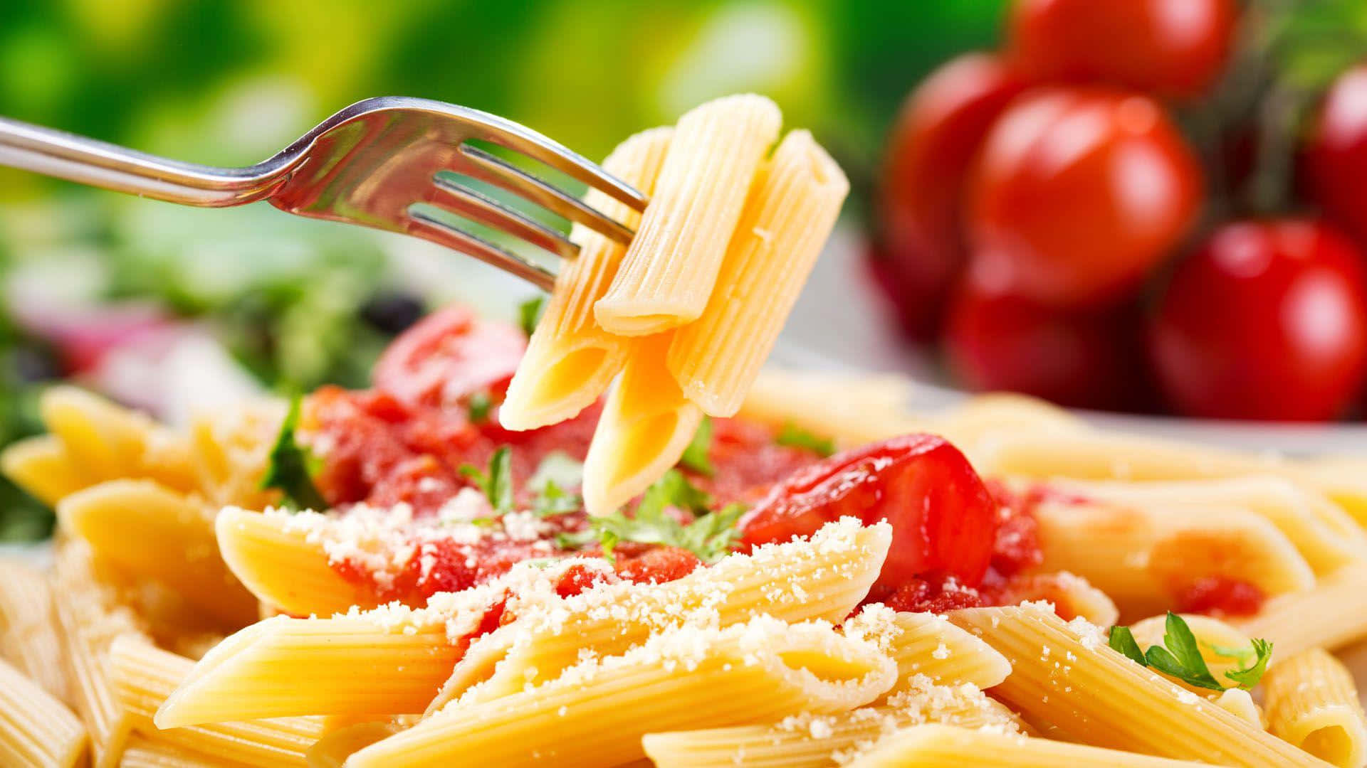 Pasta 桌布 壁紙 — 叉子正在提起沾滿鮮豔番茄醬並撒上磨碎起司的金色筆管麵，背景是模糊的綠色和紅色。