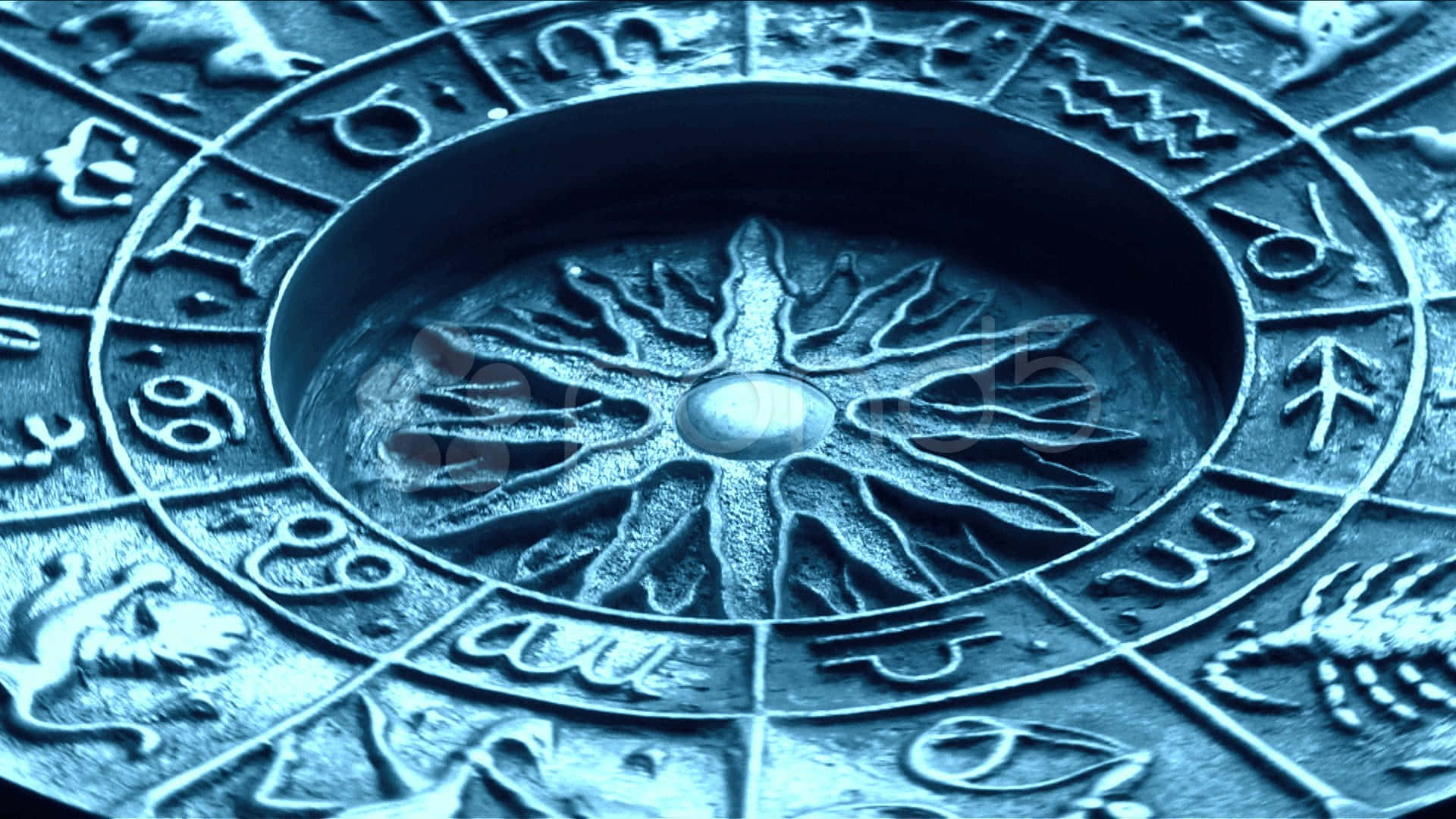 astrology 桌布 壁紙 — 古代占星黃道輪的特寫，帶有雕刻符號和中央太陽爆發圖案，在冷藍色燈光下。