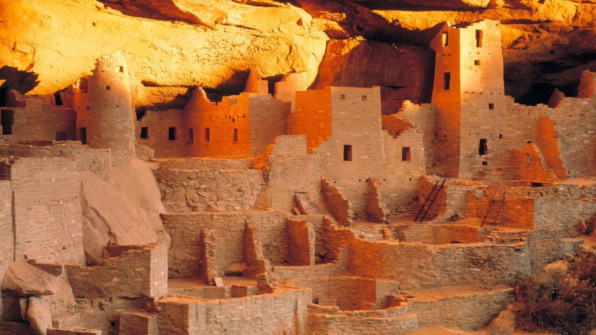 Colorado 桌布 壁紙 — 古代懸崖住所遺跡在巨大砂岩懸崖下，沐浴著金色陽光，溫暖地發光。
