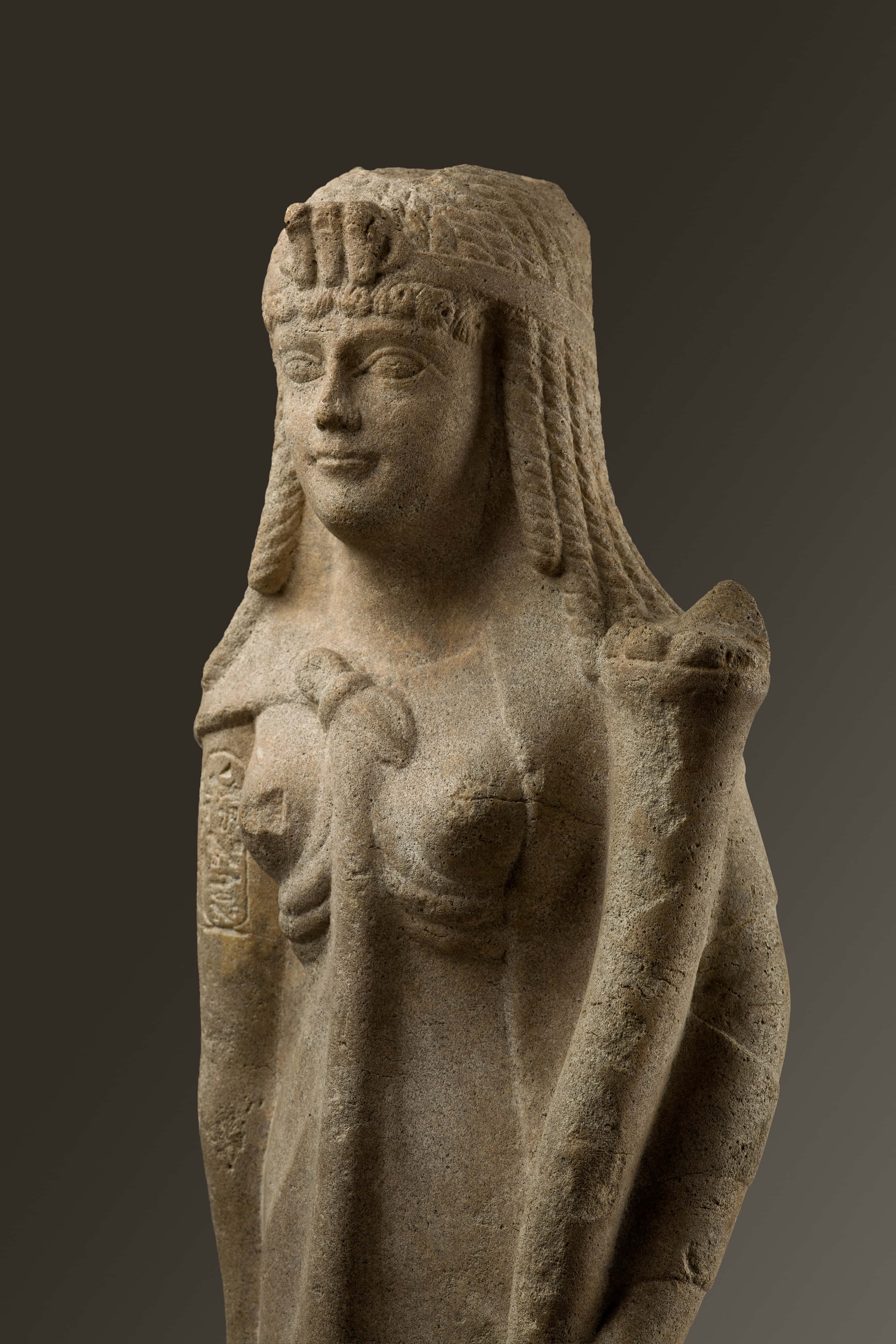 克麗奧佩特拉，尼羅河女王 壁紙 — 古代石像，一位寧靜的女性形象，編織頭髮並戴著頭飾，背景為深色漸變。