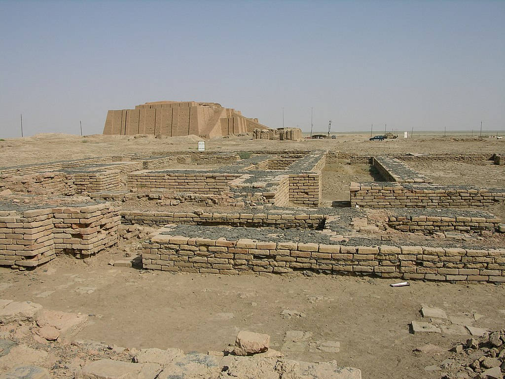 Iraq 桌布 壁紙 — 古代金字形神塔遺跡從乾旱的沙漠地形中升起，在清澈的藍天下，前景散落著磚地基。