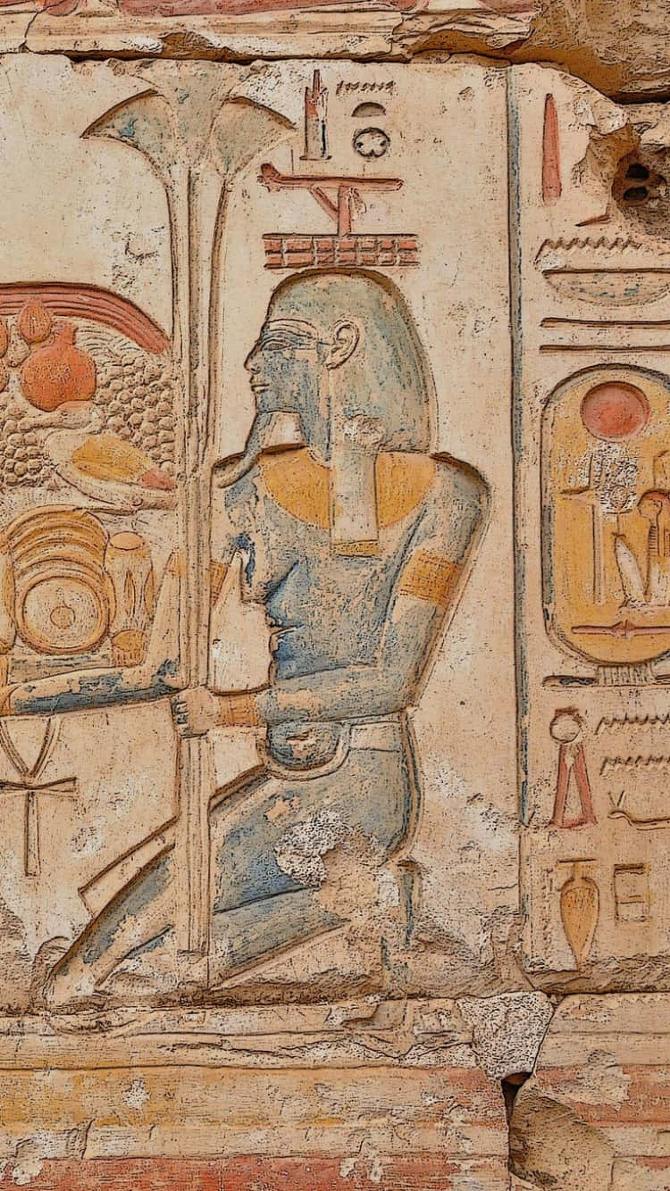 Ancient Egypt 桌布 壁紙 — 古埃及牆壁浮雕描繪一位跪著的神明，手持權杖和安卡，背景是風化的石頭和褪色的象形文字。