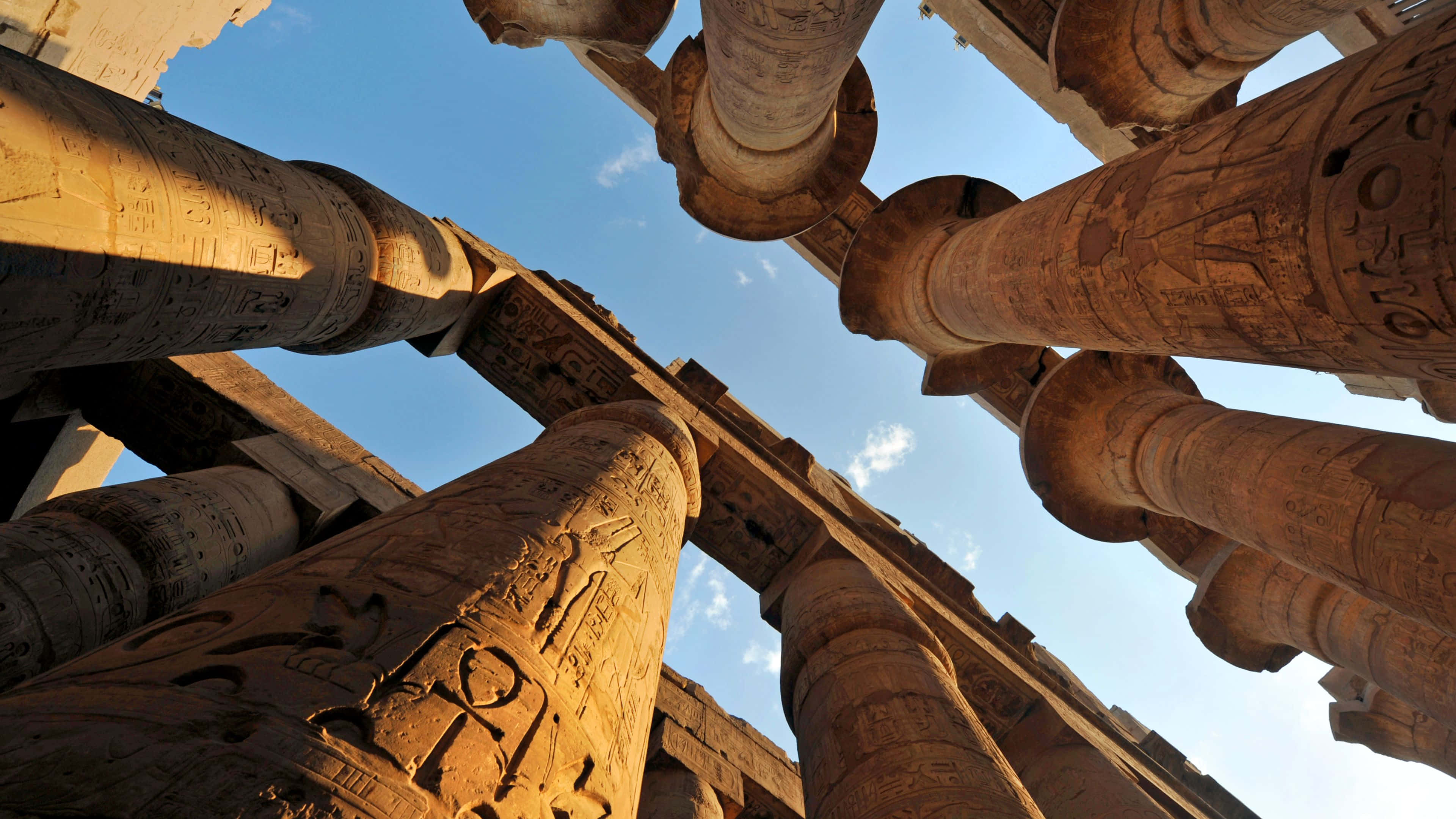 Ancient Egypt 桌布 壁紙 — 古埃及神廟的柱子雄偉地聳立在清澈的藍天下，風化的石頭上刻有複雜的象形文字。