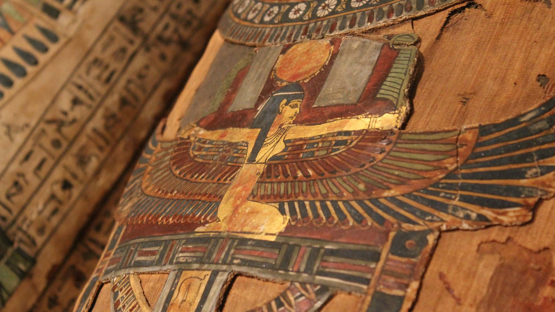 egyptian 桌布 壁紙 — 古埃及象形文字紙莎草紙的特寫，上面有色彩鮮豔的紅色、金色和藍色顏料繪製的帶翼神祇形象。