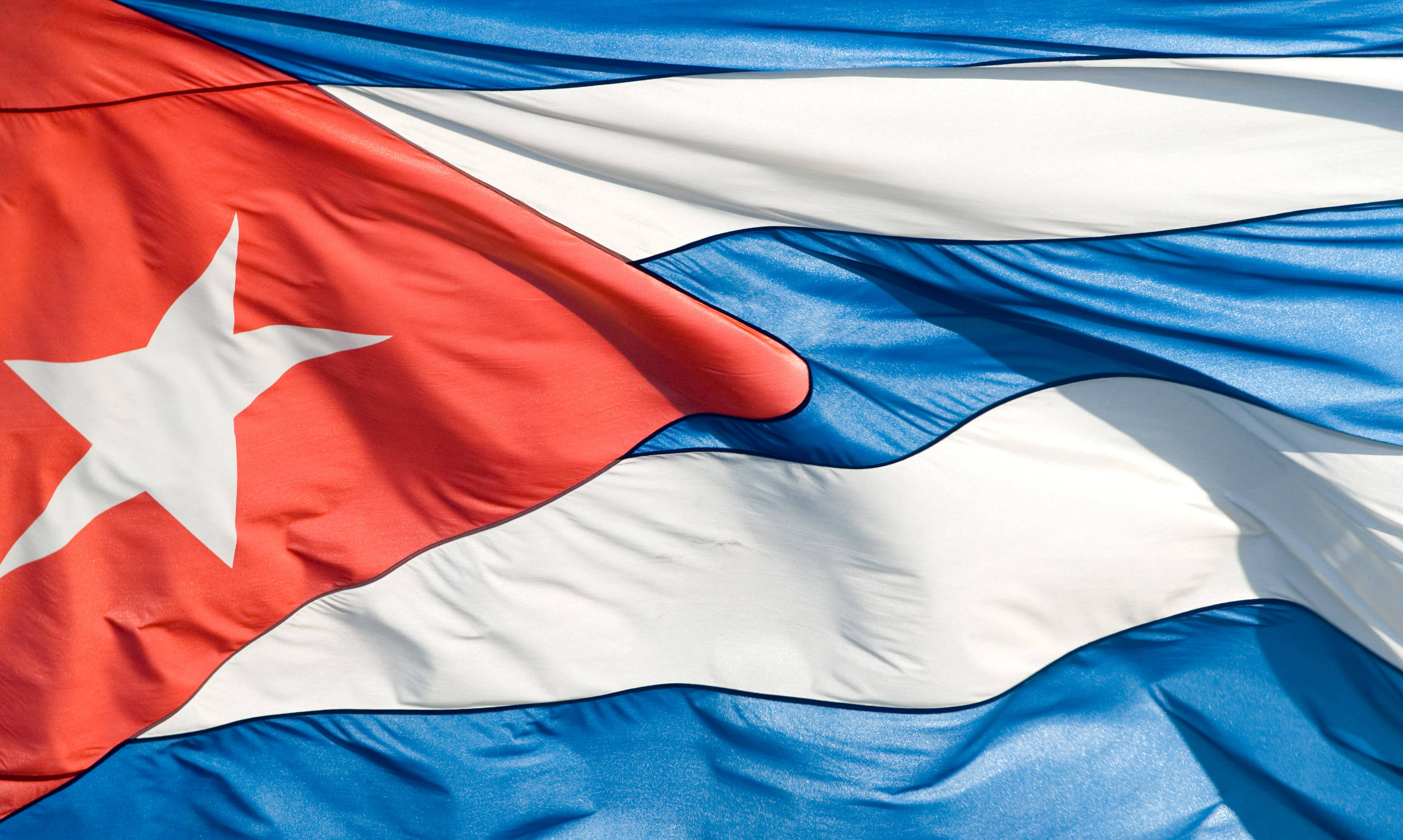 Cuban 桌布 壁紙 — 古巴國旗，帶有紅、白、藍三色條紋和一顆白色星星，在明亮的陽光下動態飄揚。