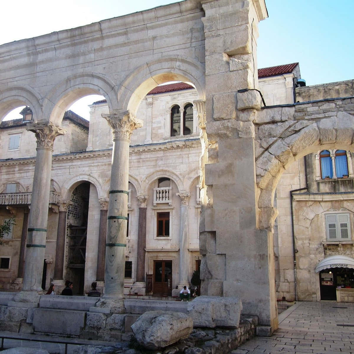 Croatia 桌布 壁紙 — 古羅馬遺址的石拱門和石柱在歷史悠久的歐洲城鎮廣場上，聳立在清澈的藍天下。