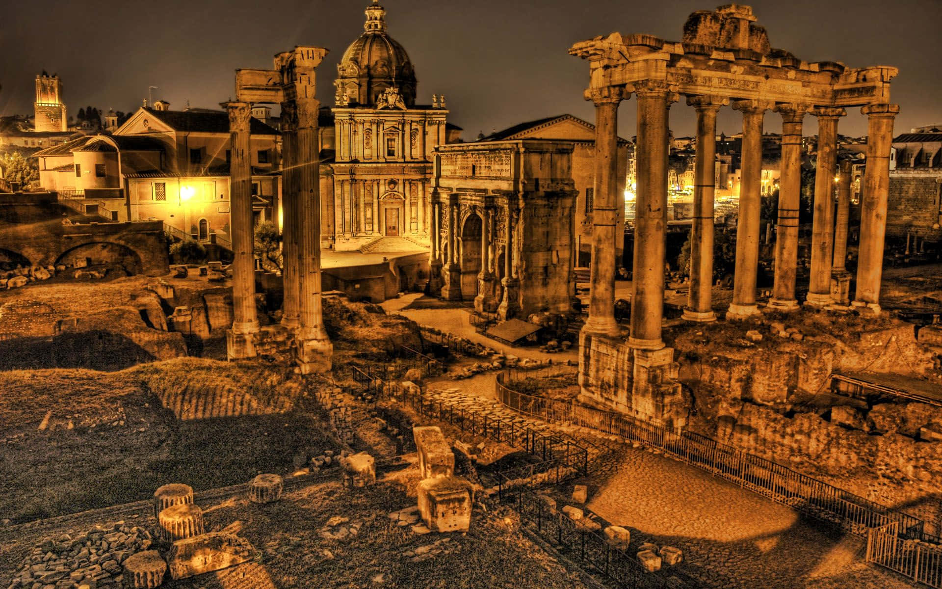 Rome 桌布 壁紙 — 古羅馬遺跡在夜燈下溫暖地發光，背景有高聳的柱子和圓頂建築。