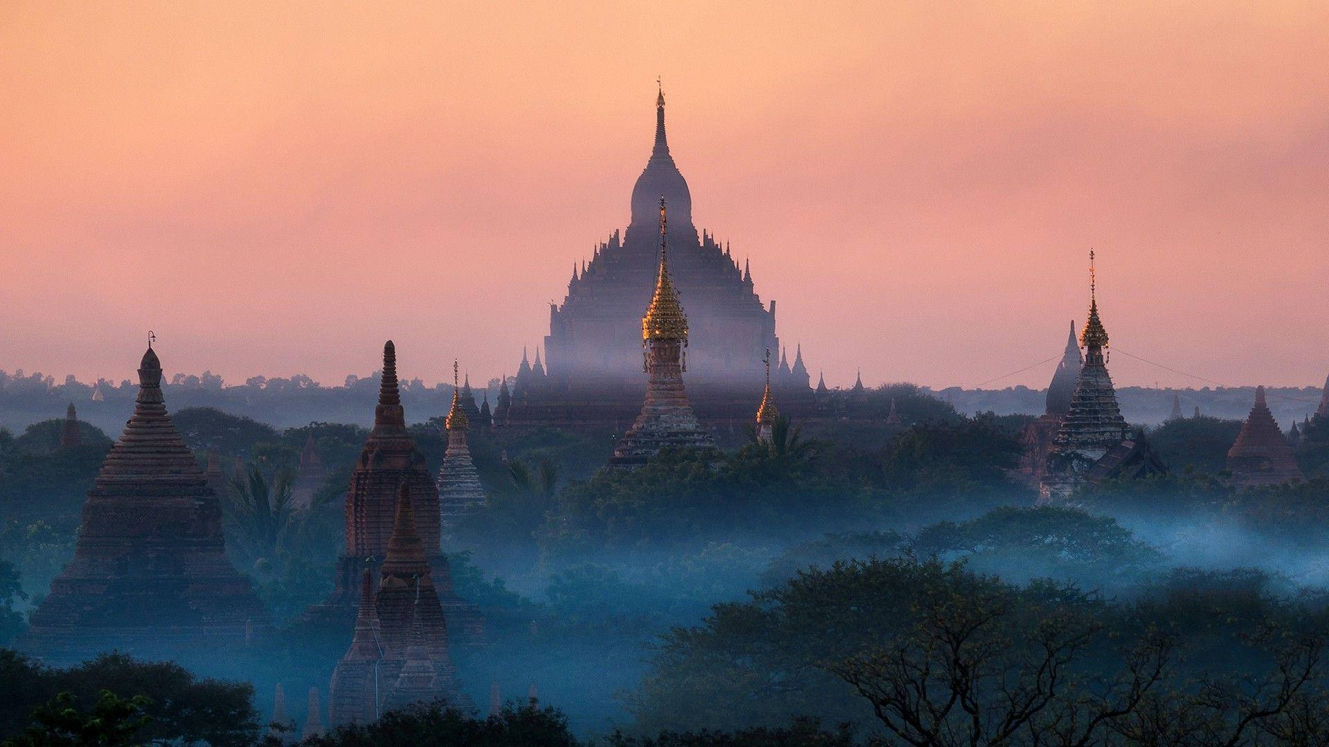 Burma 桌布 壁紙 — 古老佛塔從晨霧籠罩的叢林中升起，上方是粉橙色的天空。