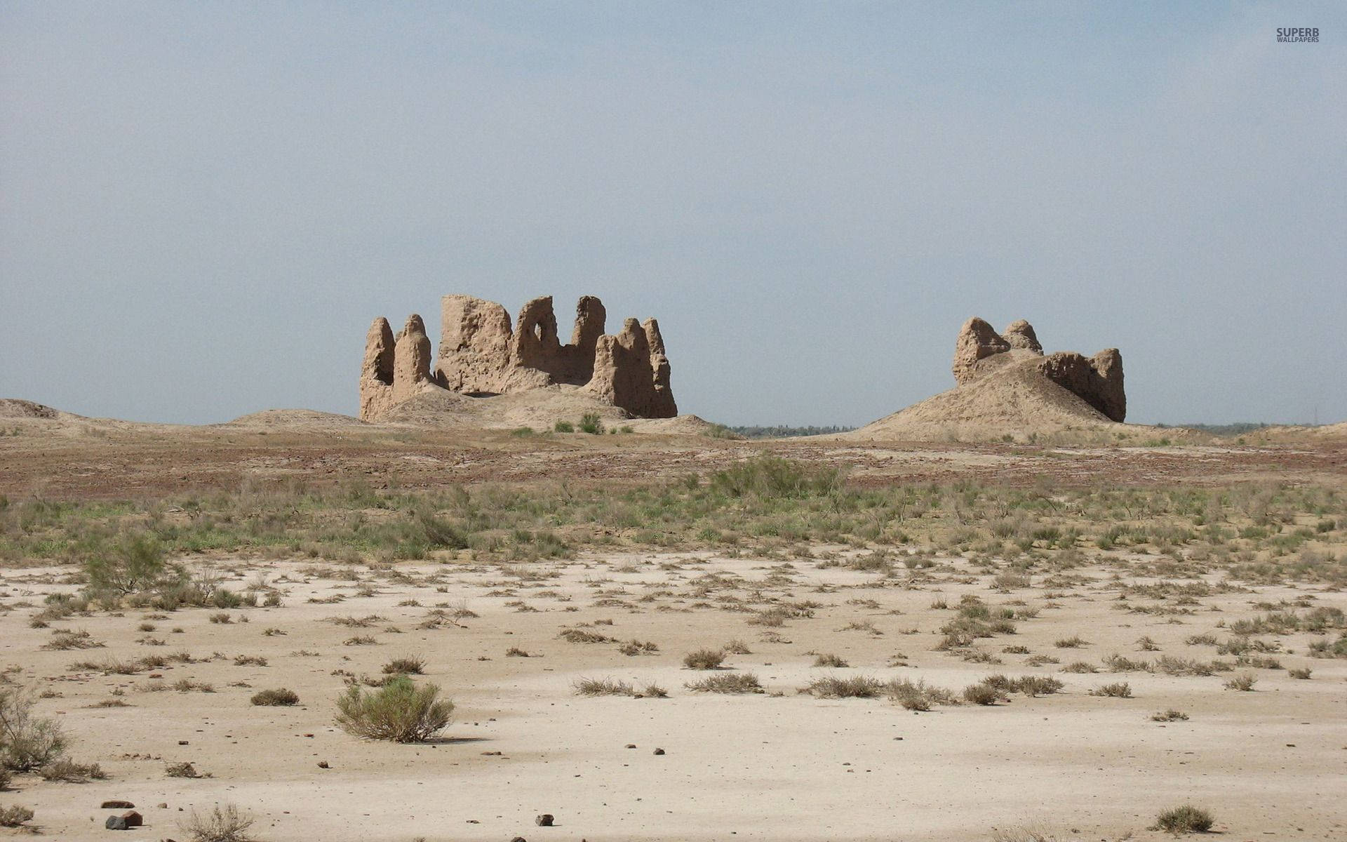Uzbekistan 桌布 壁紙 — 古老的 crumbling 石頭廢墟孤獨地矗立在廣闊乾旱的沙漠景觀中，天空蒼白。