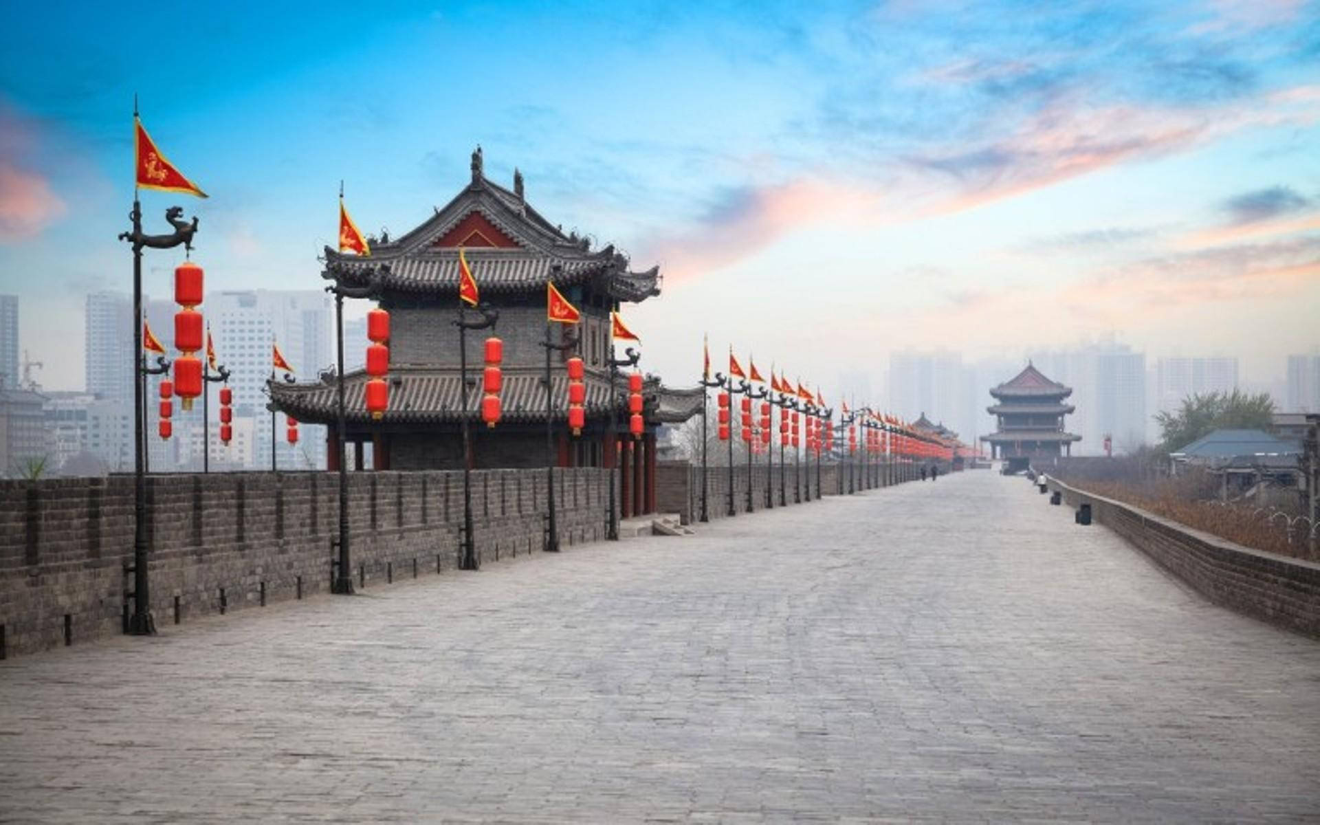 Xian 桌布 壁紙 — 古老的中國城牆上掛著紅燈籠和旗幟，在柔和的黎明天空下延伸至遠方，背景是現代建築。