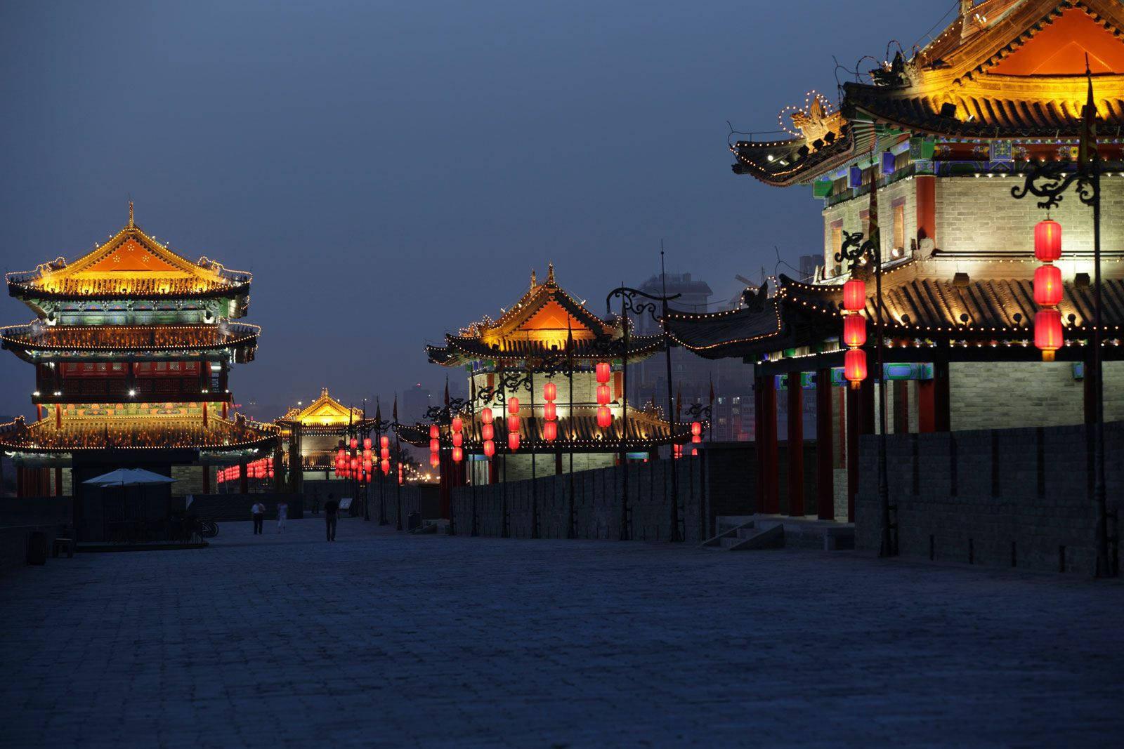 Xian 桌布 壁紙 — 古老的中國城牆在暮色中溫暖地發光，紅色燈籠照亮了傳統的塔樓和石徑。