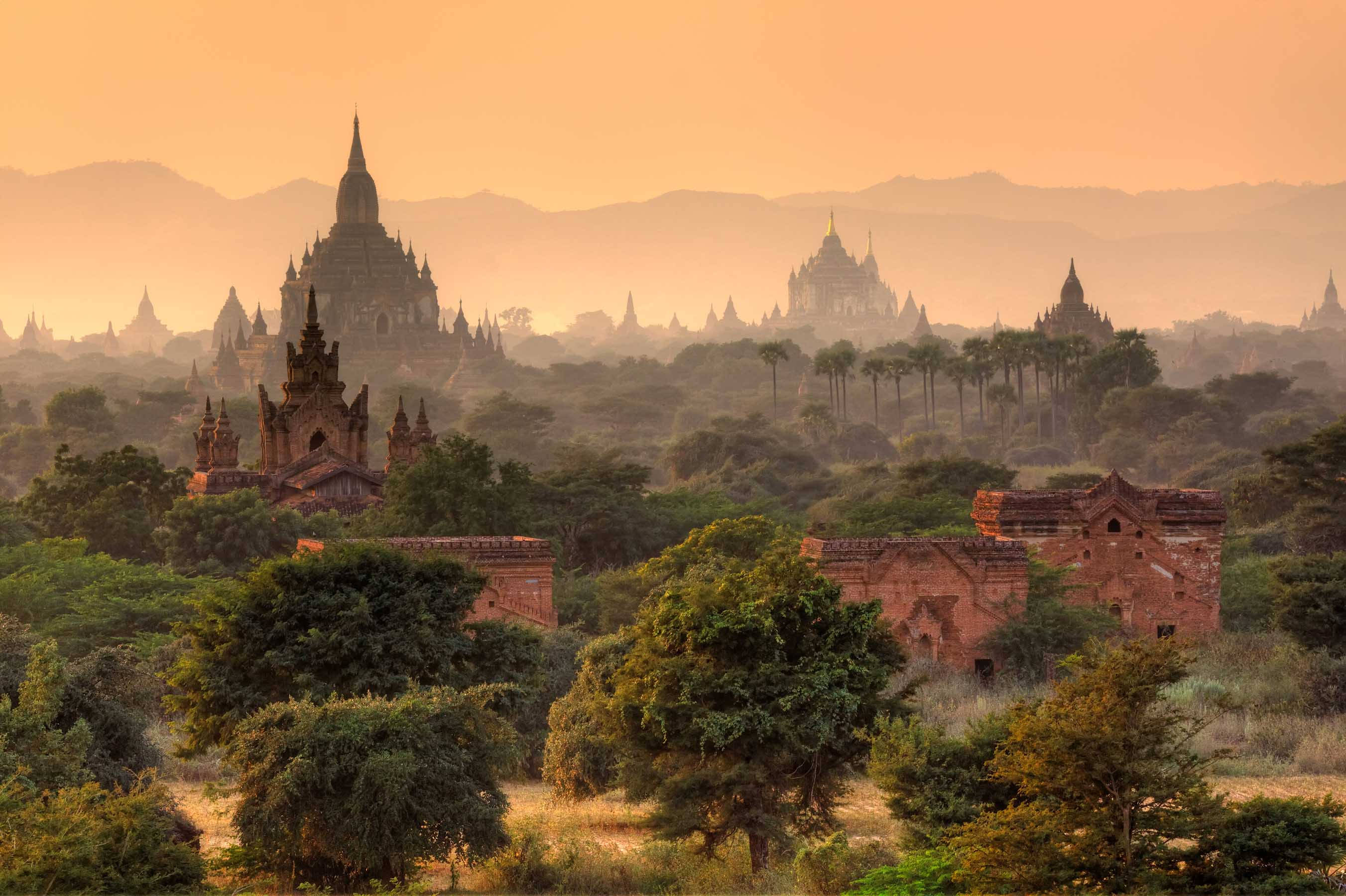 Burma 桌布 壁紙 — 古老的佛塔在金色日出時從霧氣籠罩的叢林中升起，為廢墟和遠山投下溫暖的光芒。