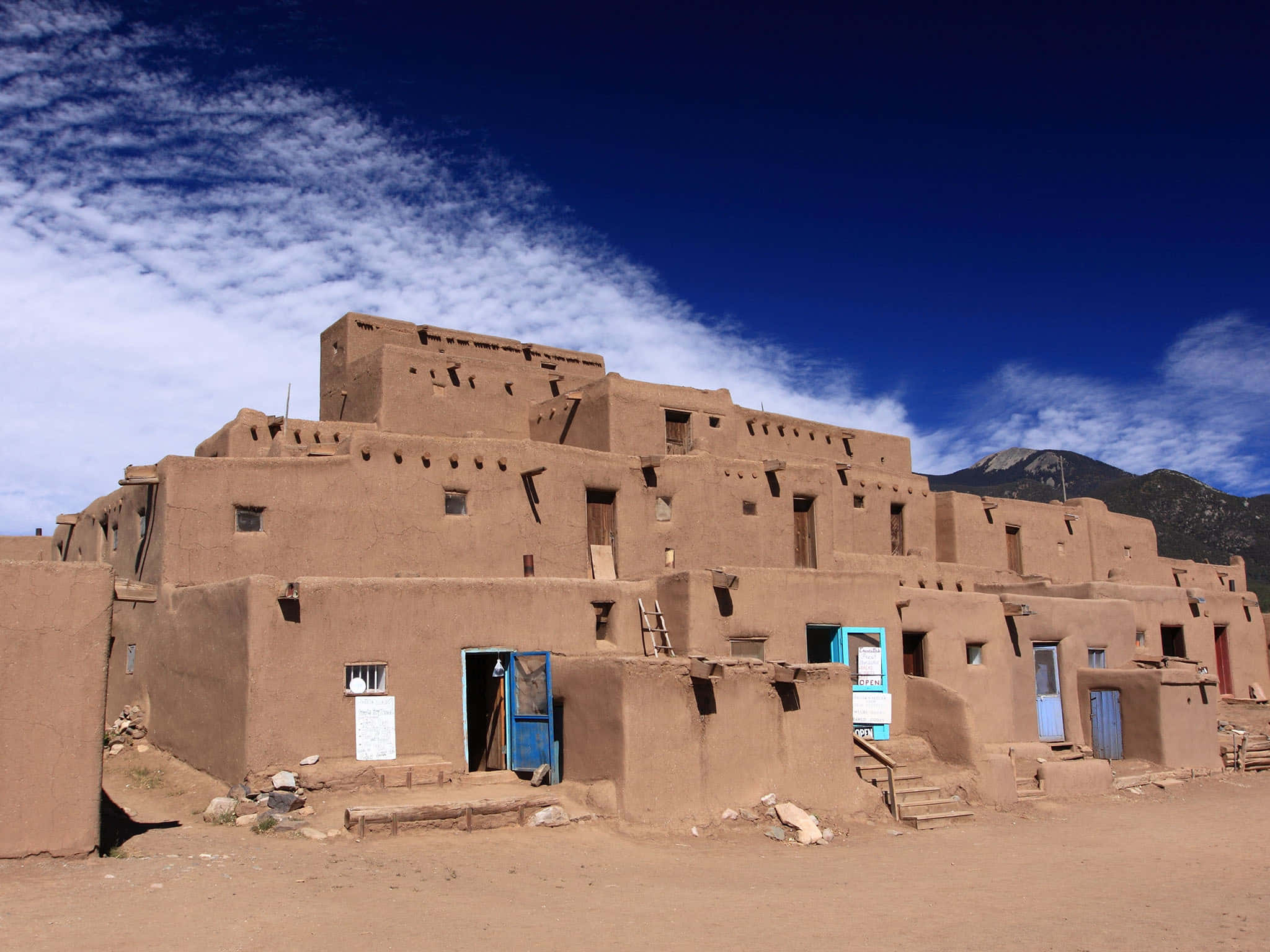 New Mexico 桌布 壁紙 — 古老的土坯普韋布洛，擁有梯田般的層次和藍色門，在藍天白雲下顯得格外醒目。