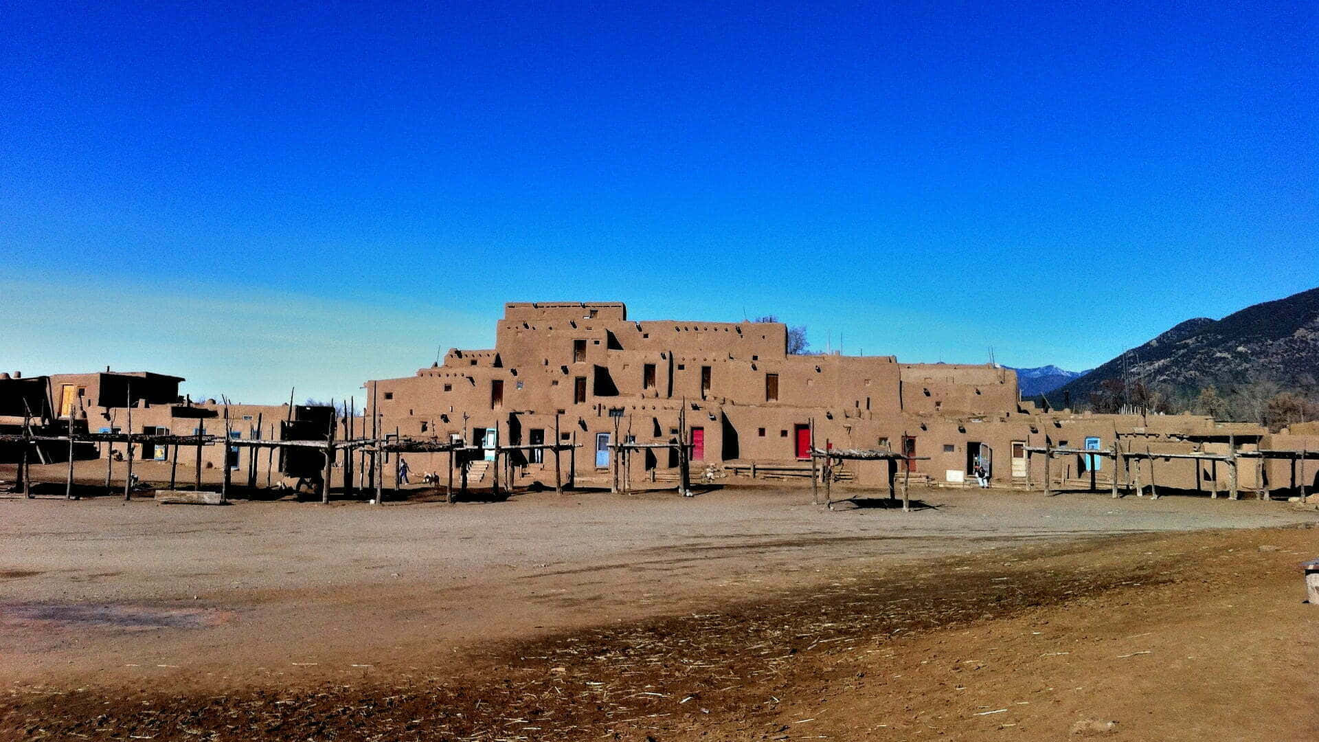 New Mexico 桌布 壁紙 — 古老的土坯普韋布洛建築矗立在清澈的藍天下，背景是遠山。