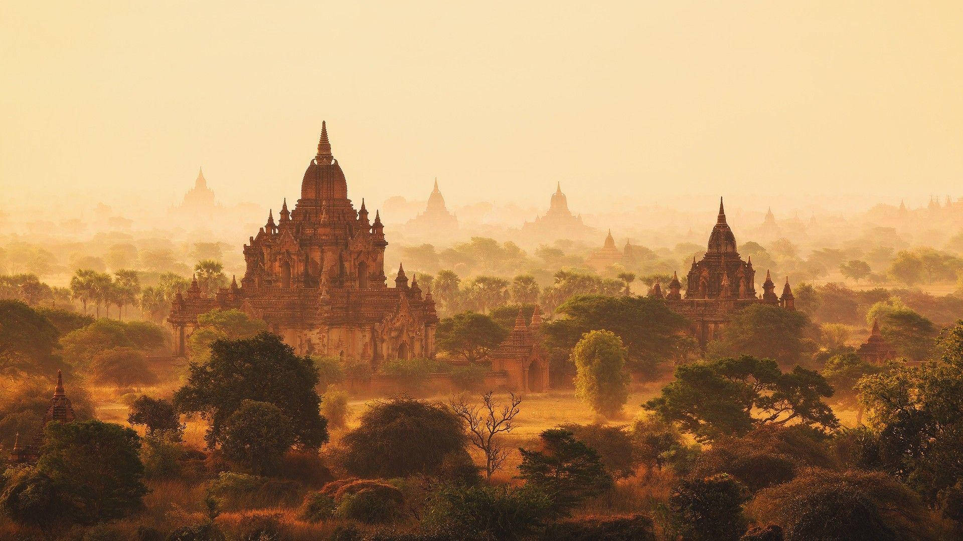 Burma 桌布 壁紙 — 古老的寶塔從霧氣瀰漫的叢林中升起，金色日出將溫暖的光芒灑在石塔尖和樹木上。