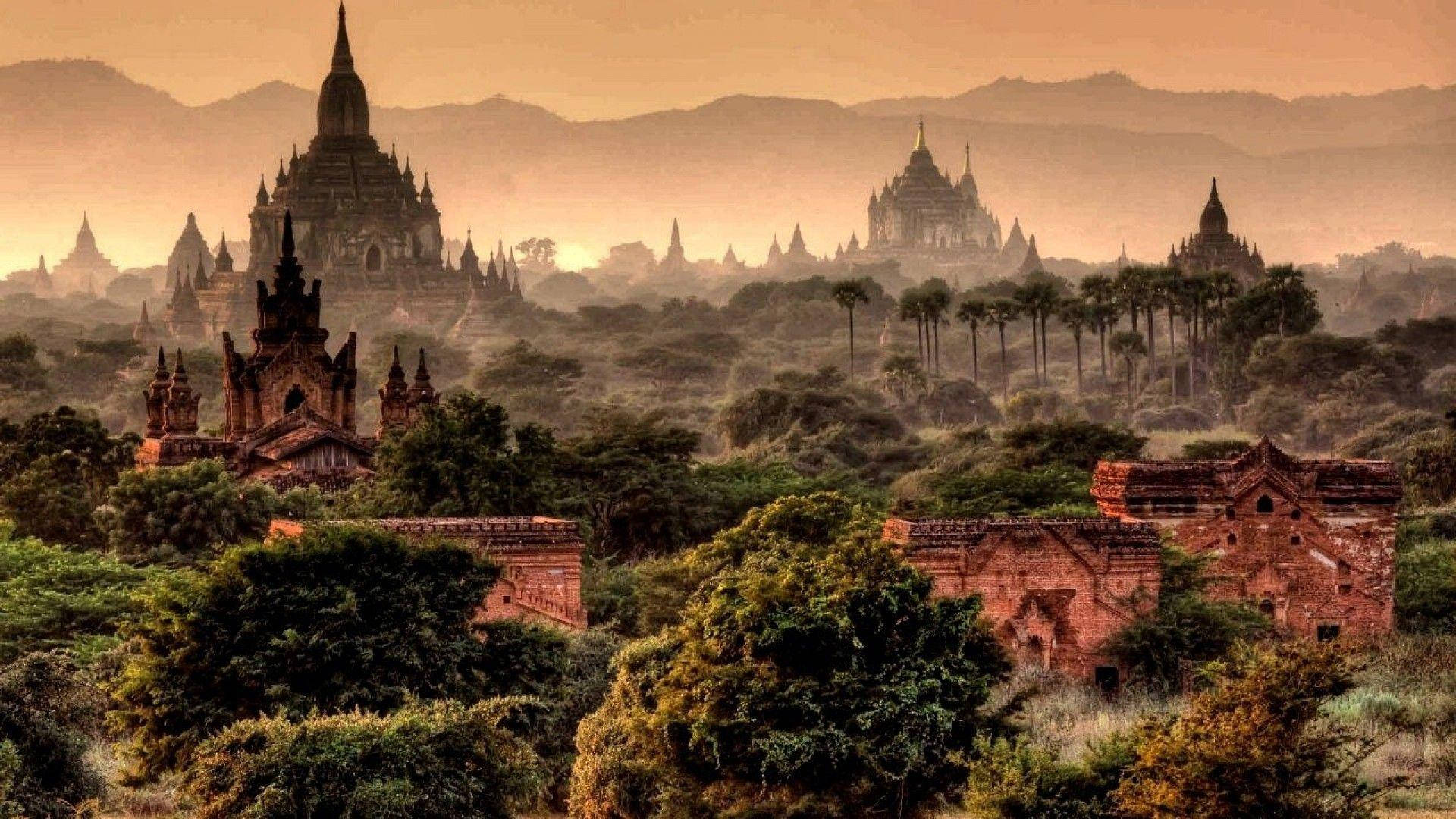 Burma 桌布 壁紙 — 古老的寶塔從霧氣瀰漫的叢林山丘中升起，溫暖的金色日出投下長長的影子。
