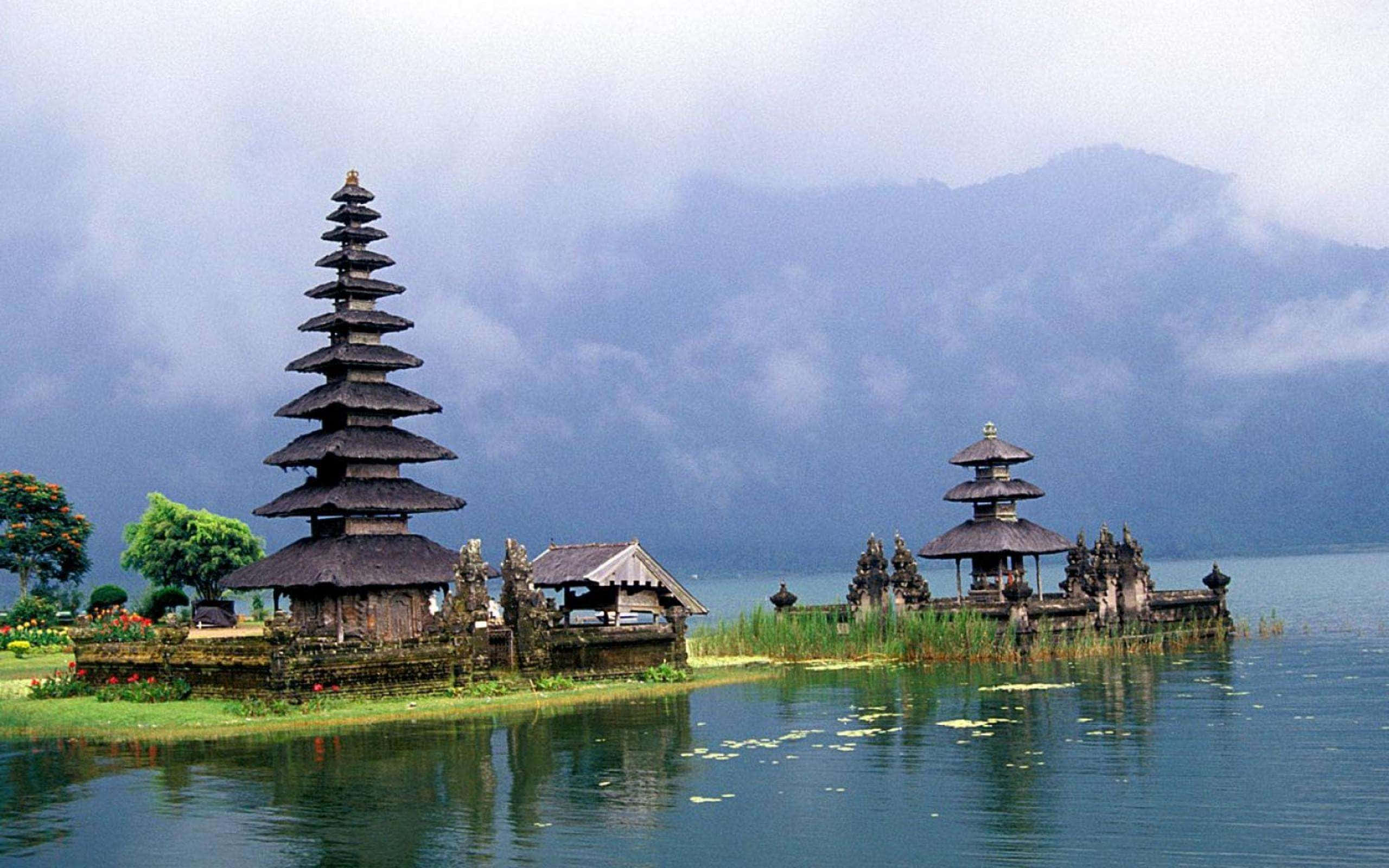 Bali Beach 桌布 壁紙 — 古老的峇里島分層寺廟從平靜的湖面升起，周圍環繞著多霧的山脈，天空多雲。
