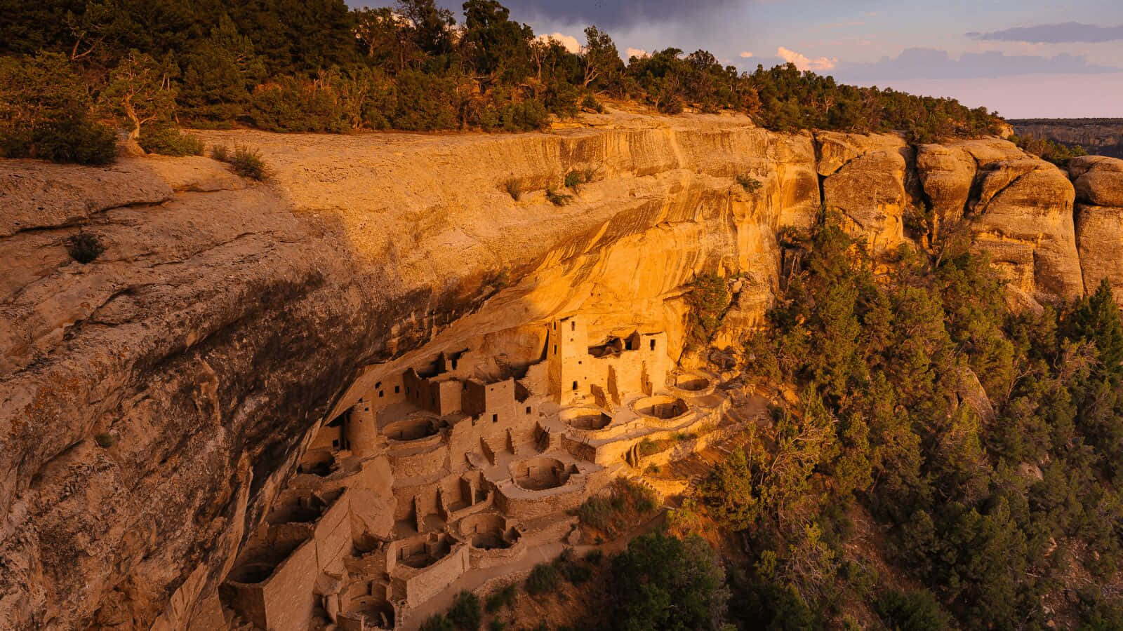 Colorado 桌布 壁紙 — 古老的懸崖住所普韋布洛遺址沐浴在金色的日落光芒中，依偎在崎嶇的峽谷壁上。