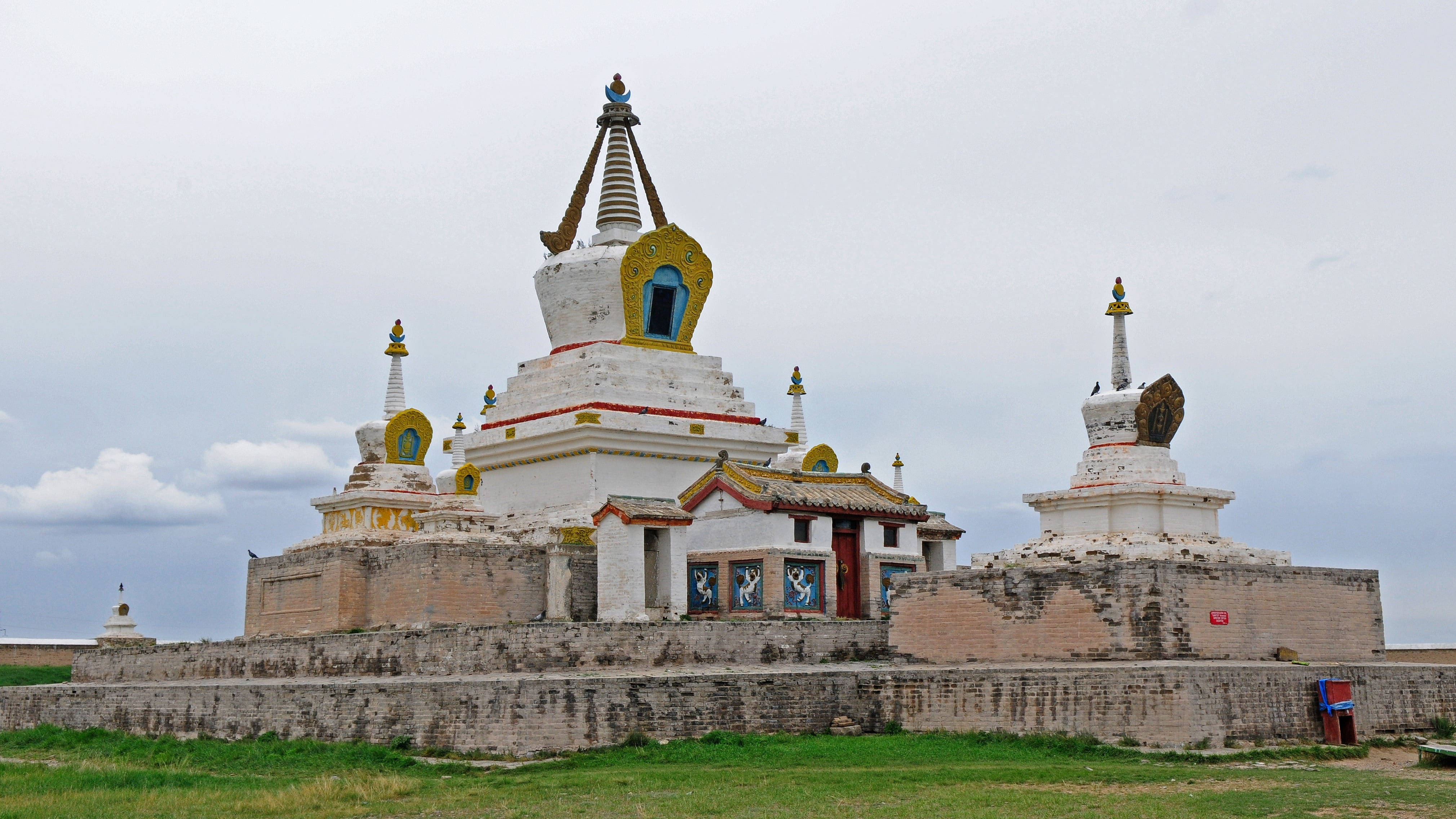 Mongolia 桌布 壁紙 — 古老的白色佛塔帶有金色點綴，在陰天天空下莊嚴地矗立於廣闊的草原上。