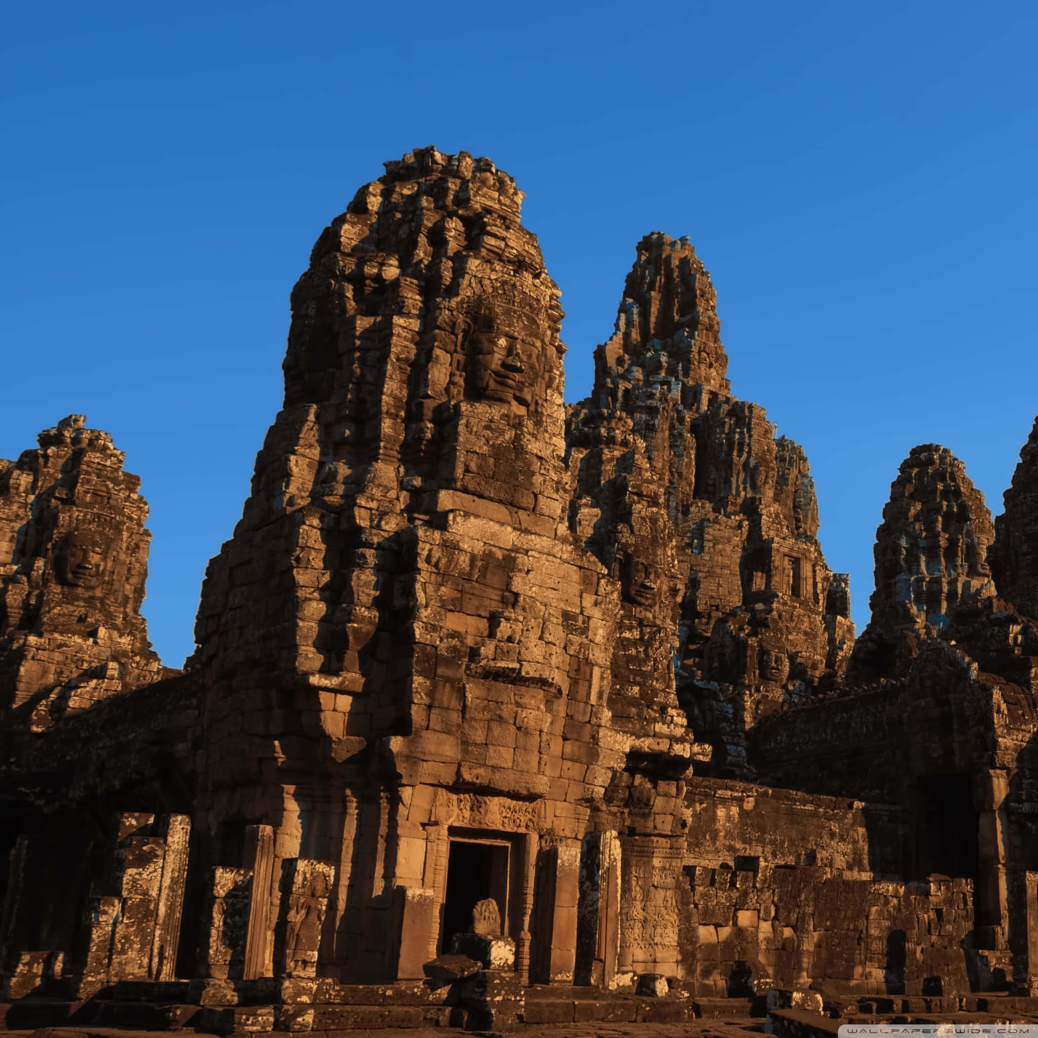 Cambodia 桌布 壁紙 — 古老的石廟塔樓雕刻著面孔，在黃金時段映襯著清澈的藍天。