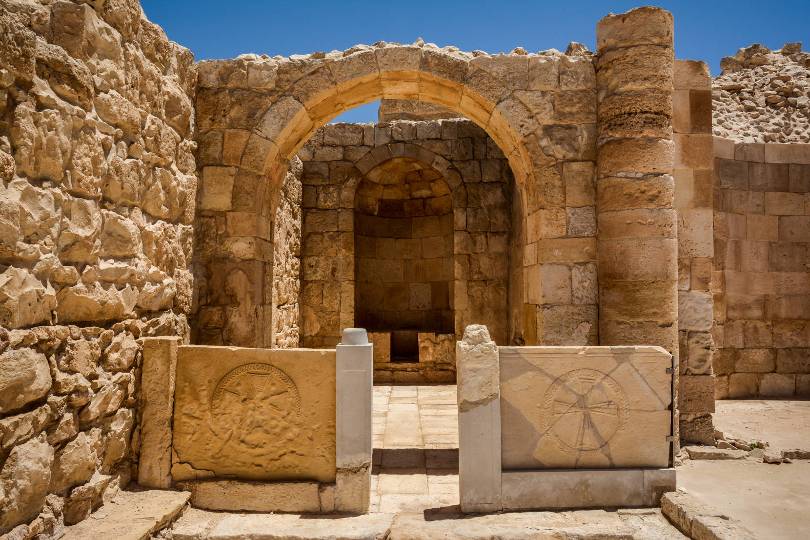 Israel 桌布 壁紙 — 古老的石拱門帶有雕刻的石碑，在明亮的藍天下矗立於陽光普照的廢墟中。