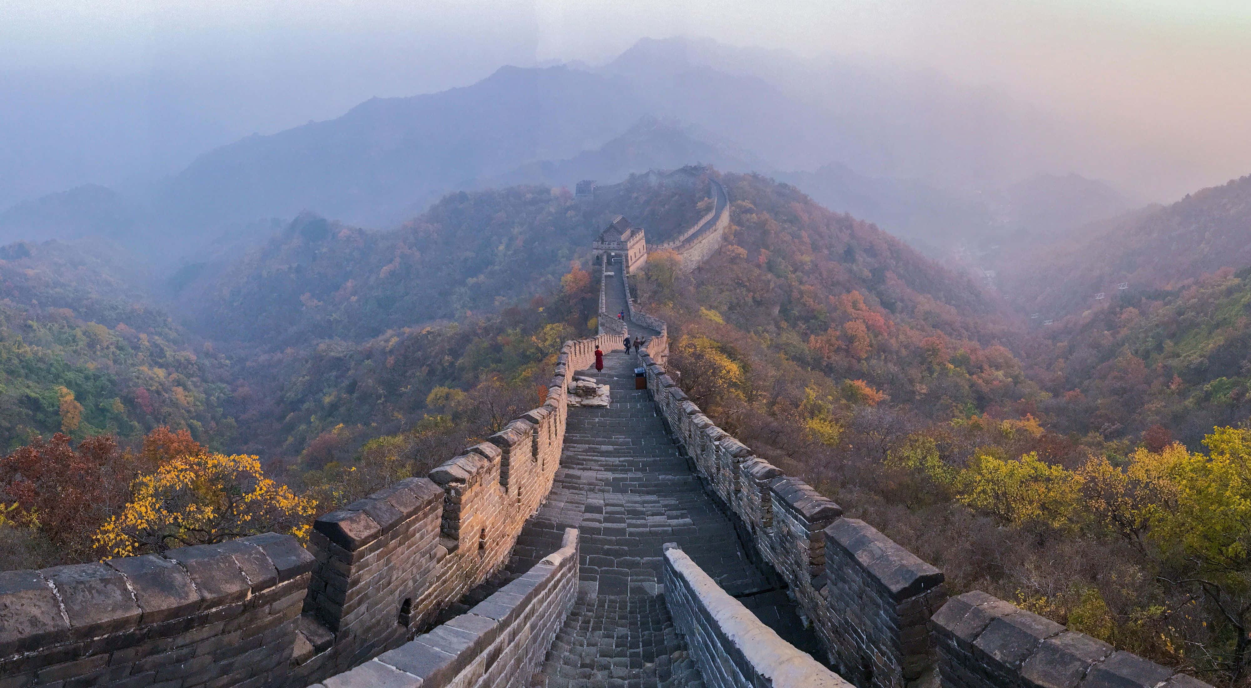 中國 桌布 壁紙 — 古老的石長城在柔和晨光下蜿蜒穿過薄霧籠罩的秋山，樹葉色彩斑斕。