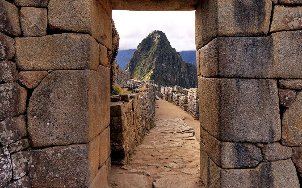 Peru 桌布 壁紙 — 古老的石門框出一條蜿蜒小徑，通往雲天下標誌性的馬丘比丘山頂。