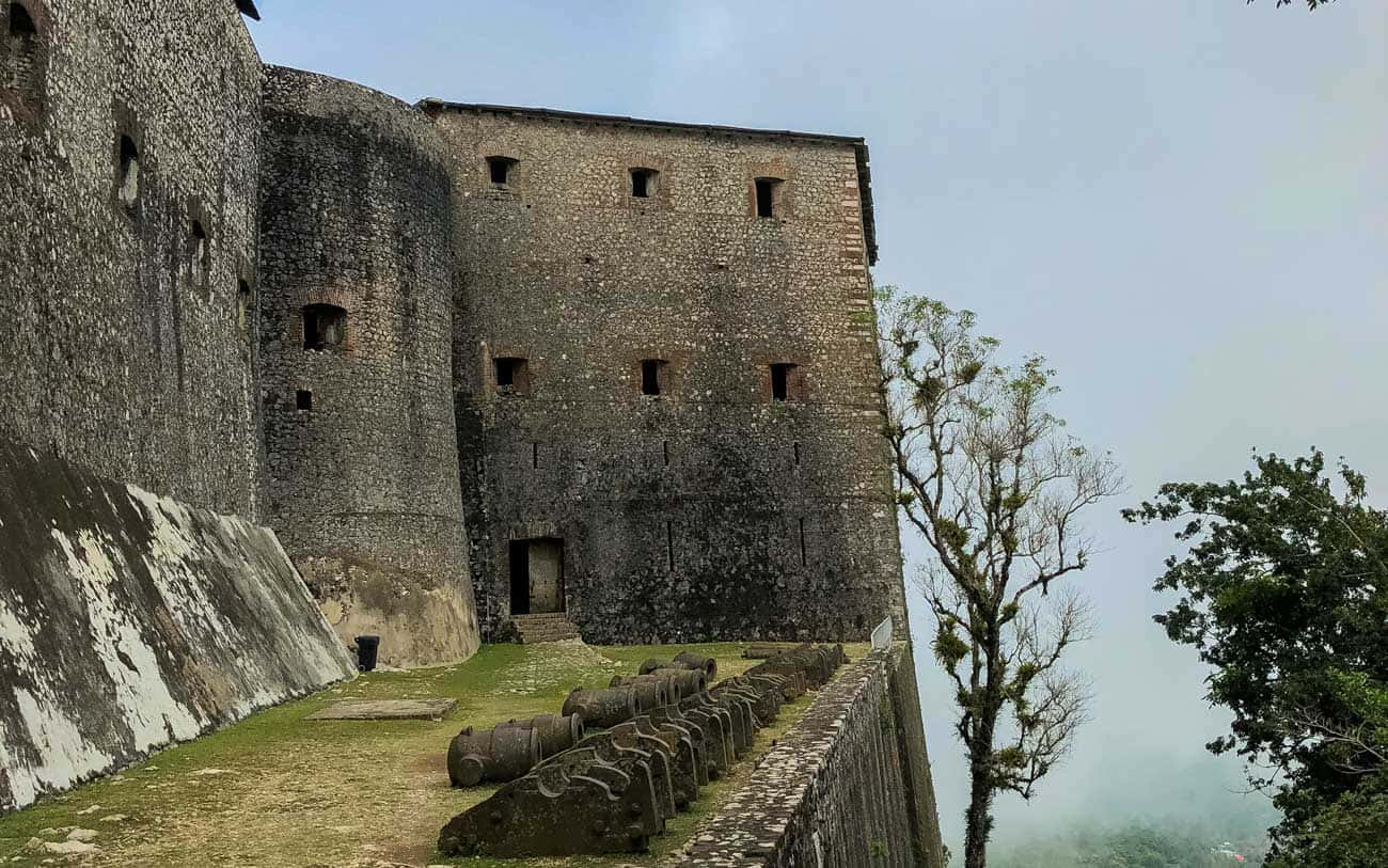 Fortress 桌布 壁紙 — 古老的石頭堡壘，風化的城牆和大砲排列在霧氣瀰漫的山坡上，天空多雲。