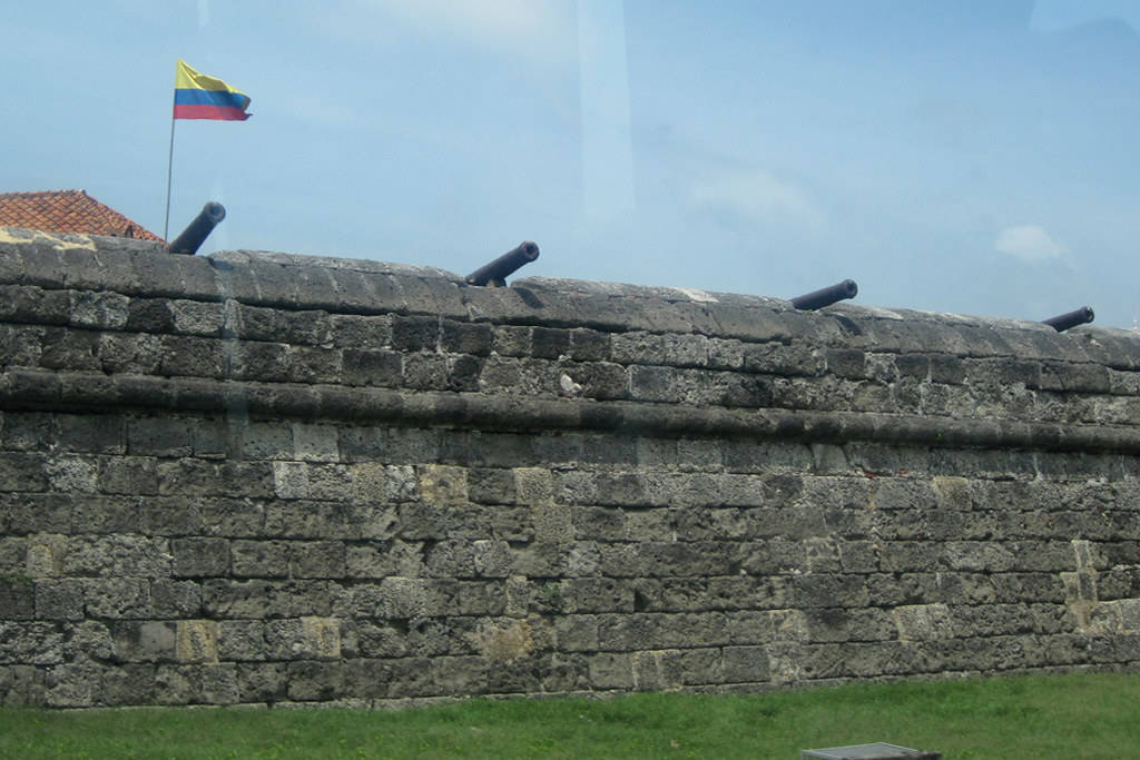 Colombia 桌布 壁紙 — 古老的石頭堡壘牆，配有大砲，以及一面在清澈藍天下飄揚的哥倫比亞國旗。
