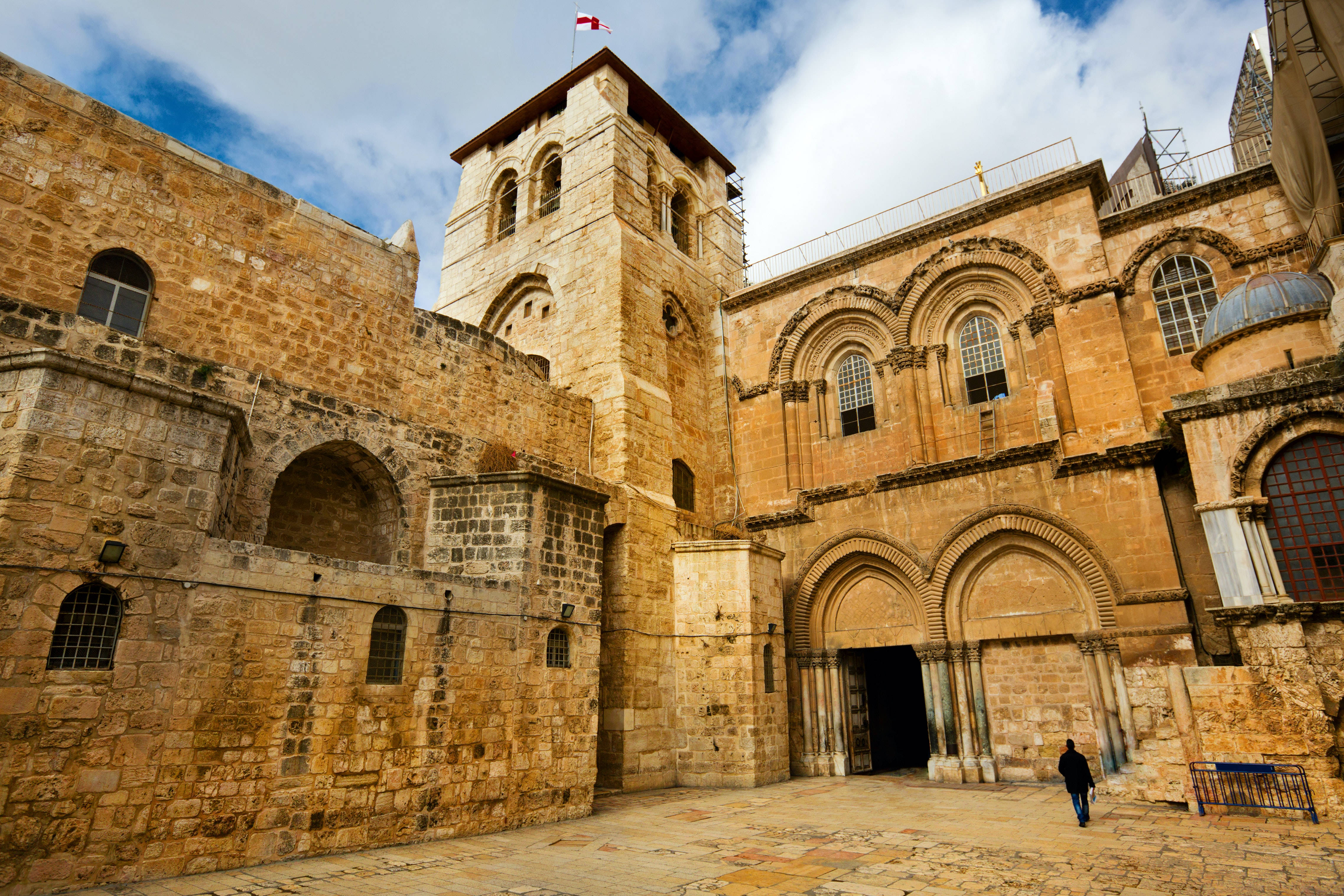 Israel 桌布 壁紙 — 古老的石頭教堂，有拱形門廊和塔頂上的旗幟，天空部分多雲。