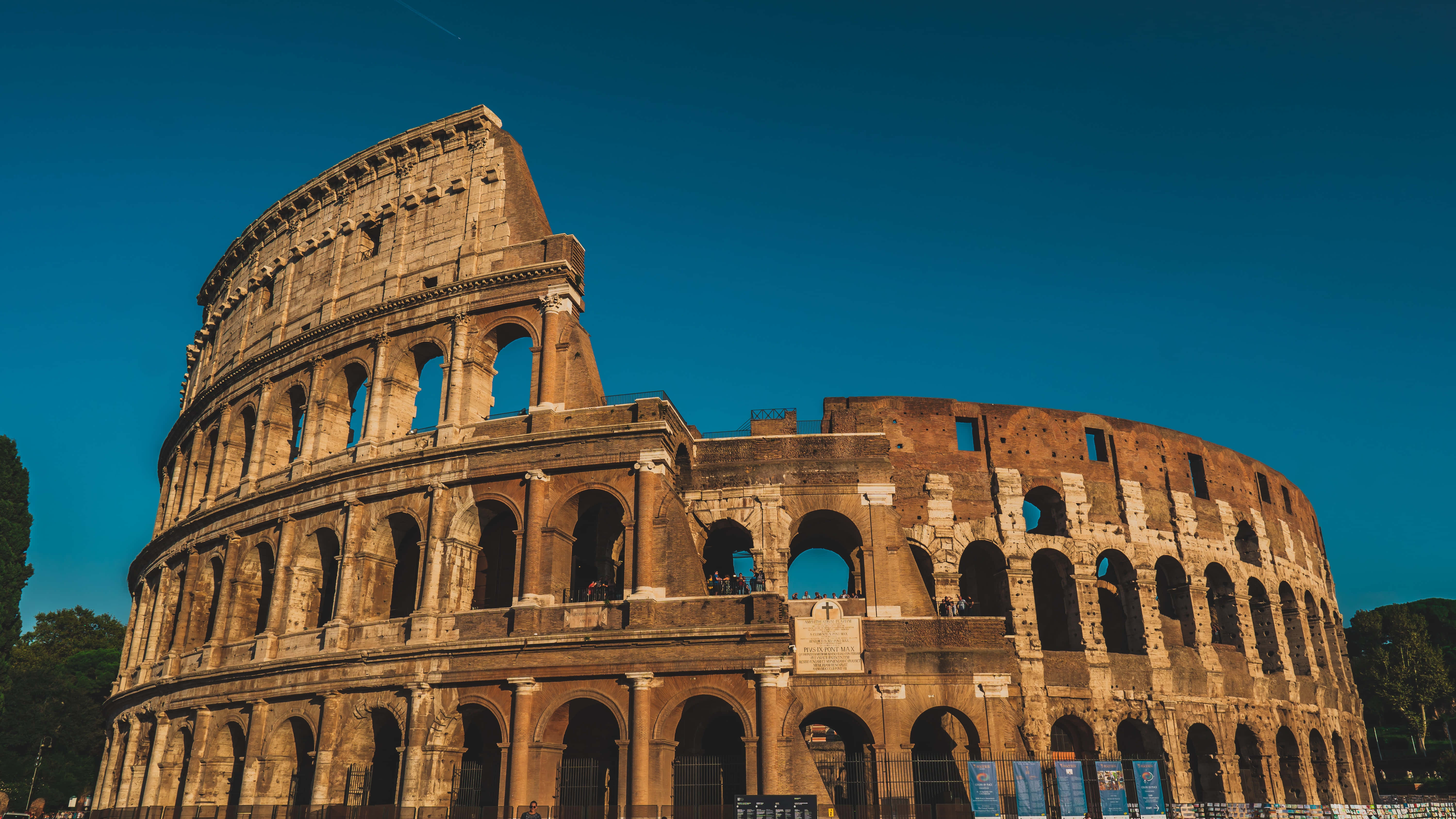 Ancient Roman Desktop 桌布 壁紙 — 古老的羅馬競技場在清澈的藍天下雄偉矗立，溫暖的陽光突顯其風化的石拱門。