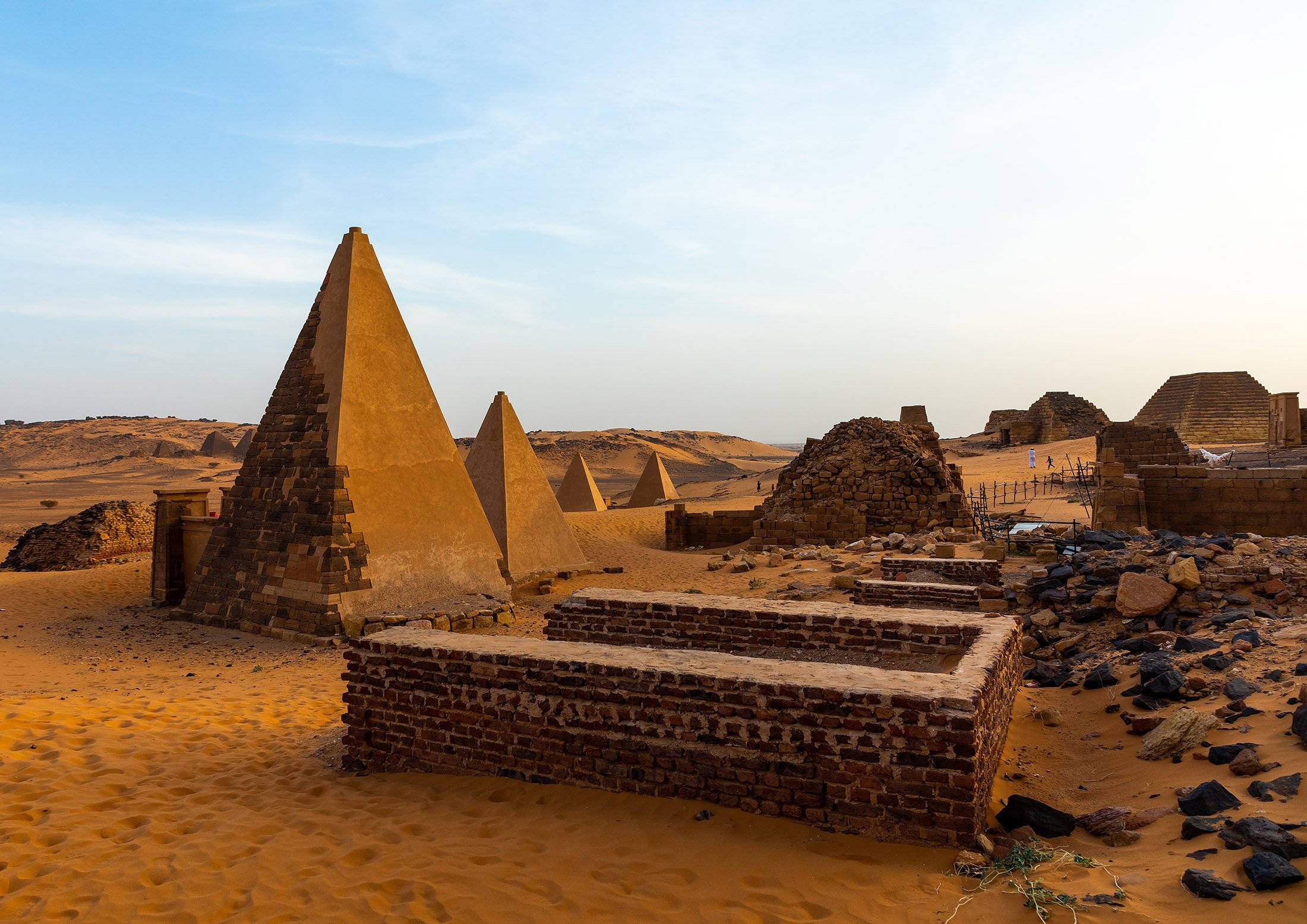Sudan 桌布 壁紙 — 古老的金字塔和磚砌遺跡在日落時分柔和的藍天下，莊嚴地矗立在廣闊的金色沙漠中。