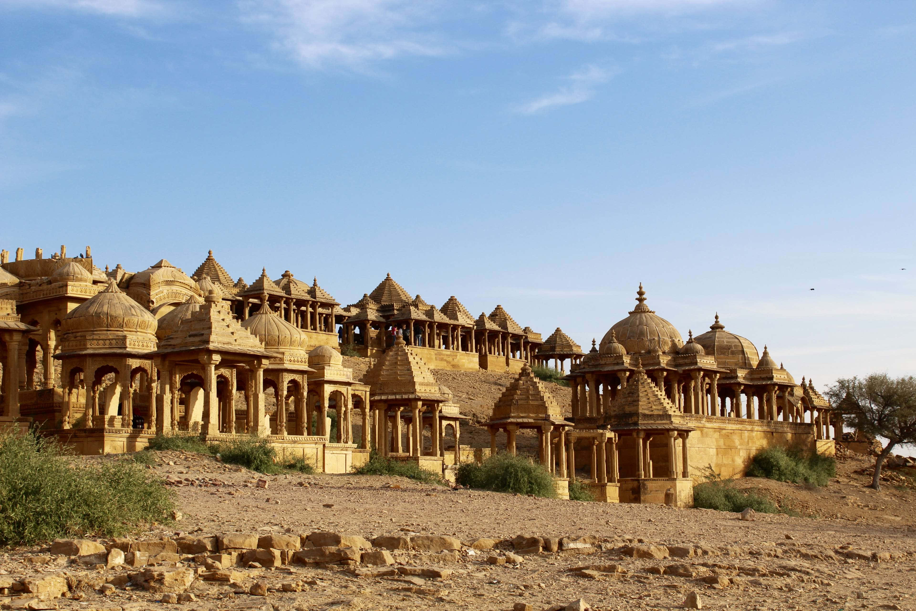 Rajasthan 桌布 壁紙 — 古老的金色砂岩寺廟，帶有圓頂和拱門，在晴朗的藍天下從乾燥的沙漠地形中升起。