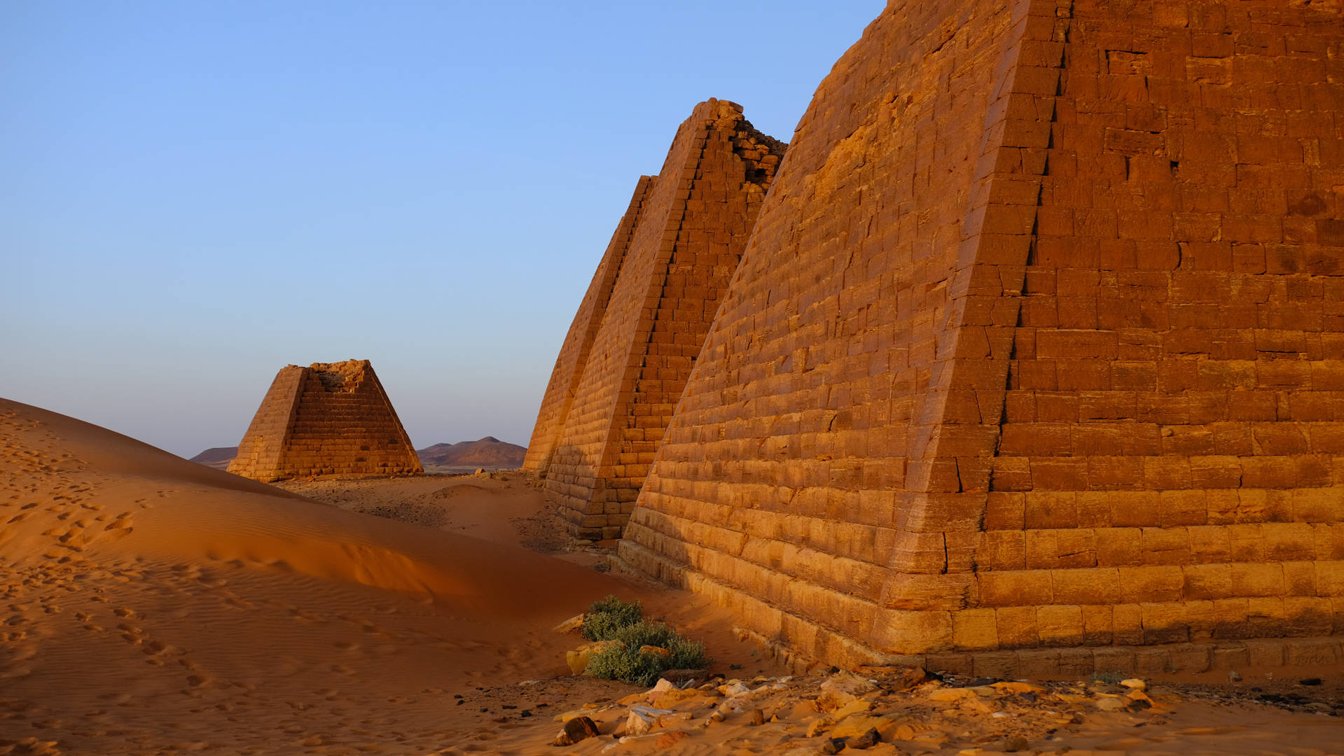 Sudan 桌布 壁紙 — 古老的階梯金字塔在夕陽下從金色沙漠中升起，天空清澈湛藍。